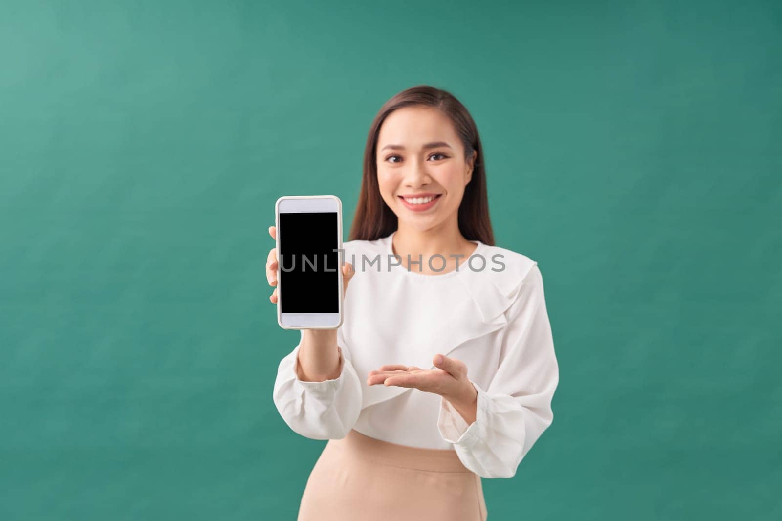 Young beautiful attractive Asian woman show blank screen mobile phone isolated on green background by makidotvn