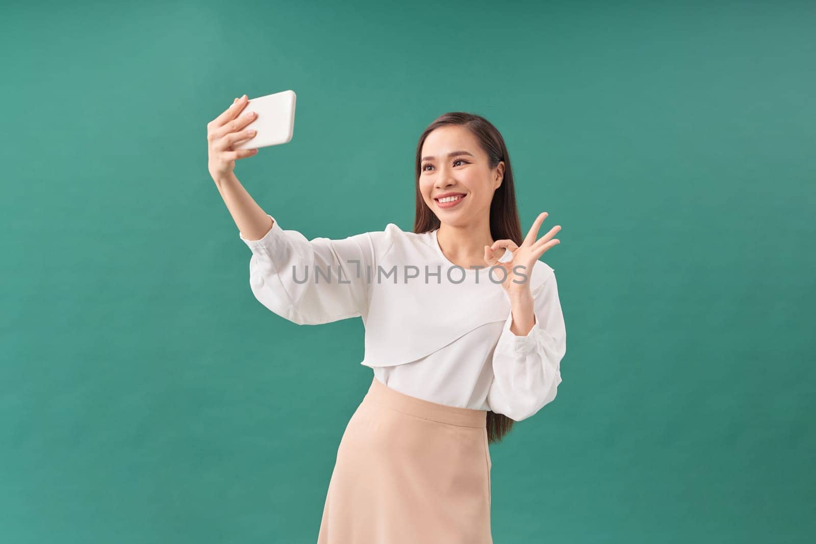 Smiling young girl making selfie photo on smartphone over green background by makidotvn