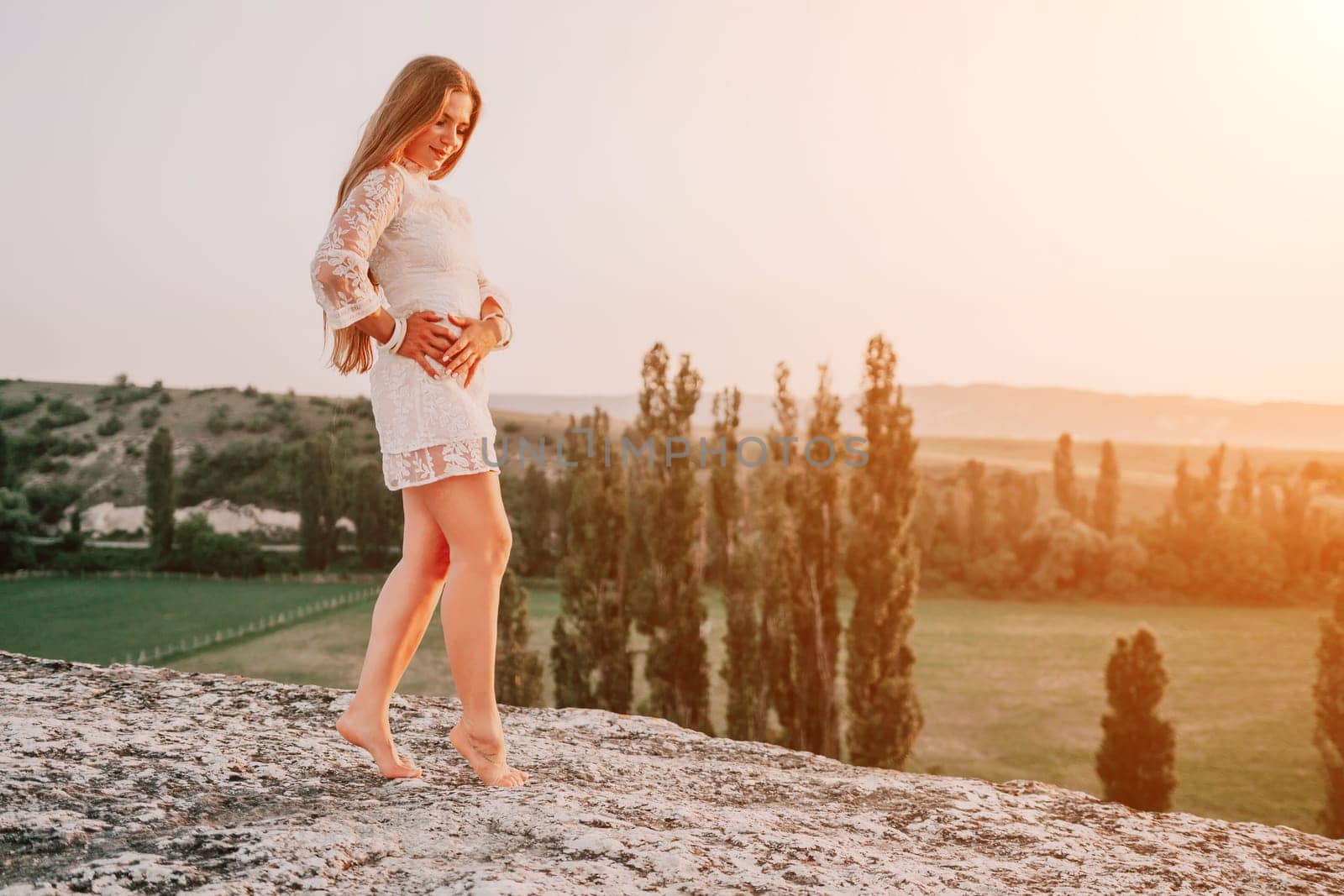 Romantic beautiful bride in white dress posing with sea and mountains in background. Stylish bride standing back on beautiful landscape of sea and mountains on sunset