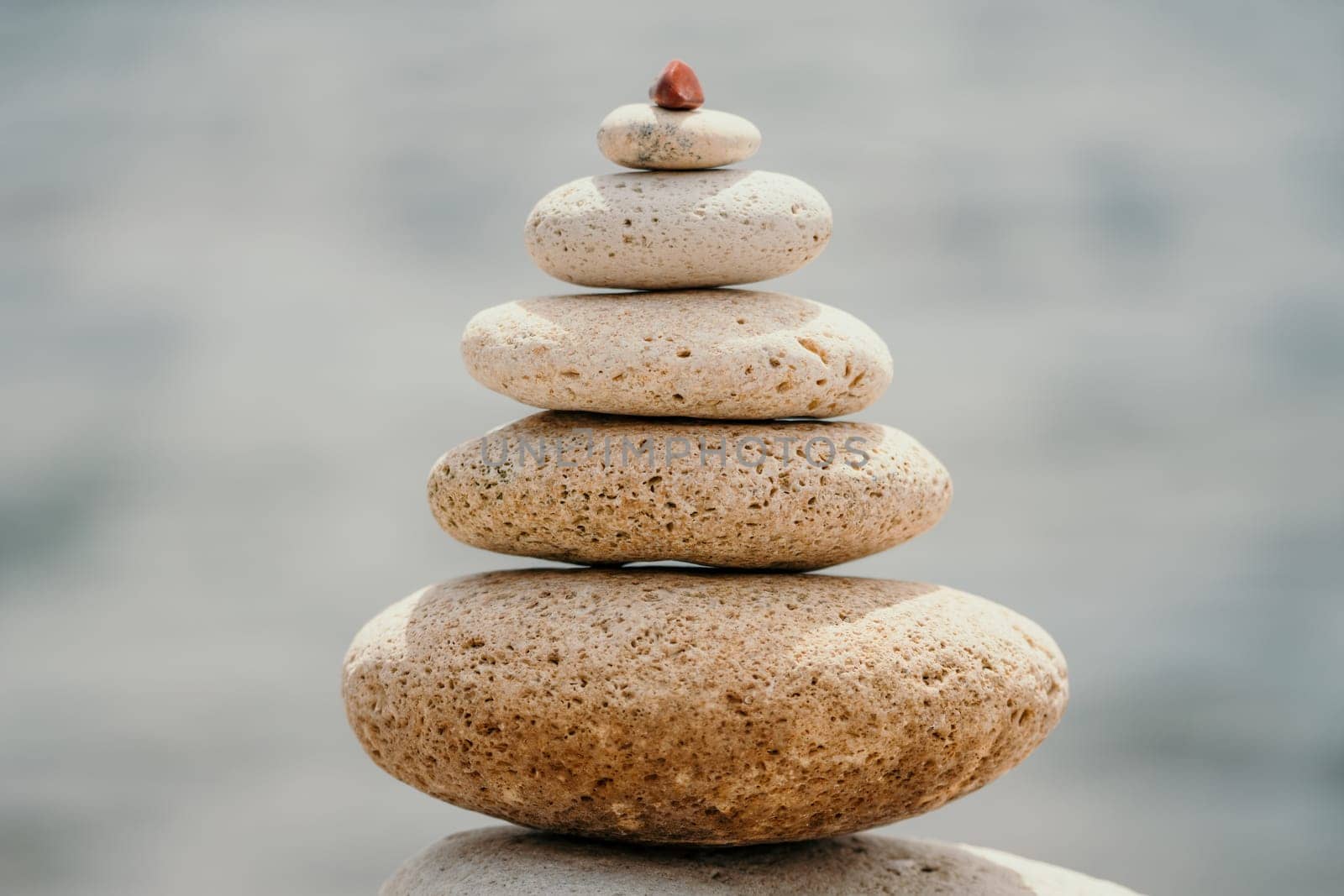 Balanced rock pyramid on sea pebbles beach, at sunset. Golden sea bokeh on background. Selective focus, zen stones on sea beach, meditation, spa, harmony, calm, balance concept by panophotograph