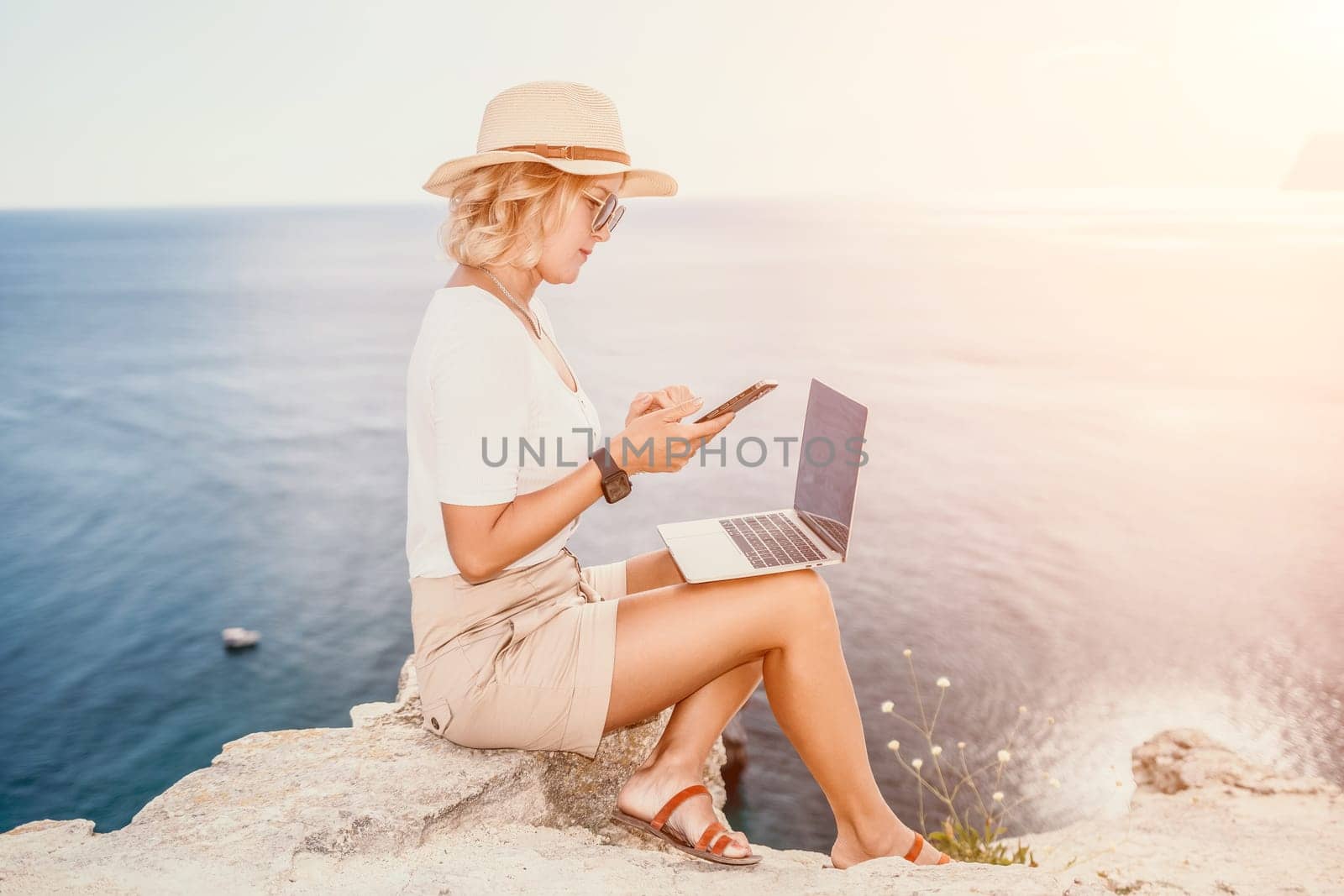 Digital nomad, Business woman working on laptop by the sea. Pretty lady typing on computer by the sea at sunset, makes a business transaction online from a distance. Freelance, remote work on vacation by panophotograph