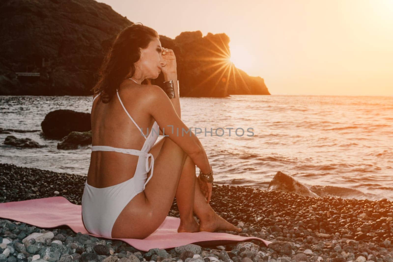 Woman sea yoga. Happy woman meditating in yoga pose on sunset beach, ocean and rock mountains. Motivation and inspirational fit and exercising. Healthy lifestyle outdoors in nature, fitness concept. by panophotograph