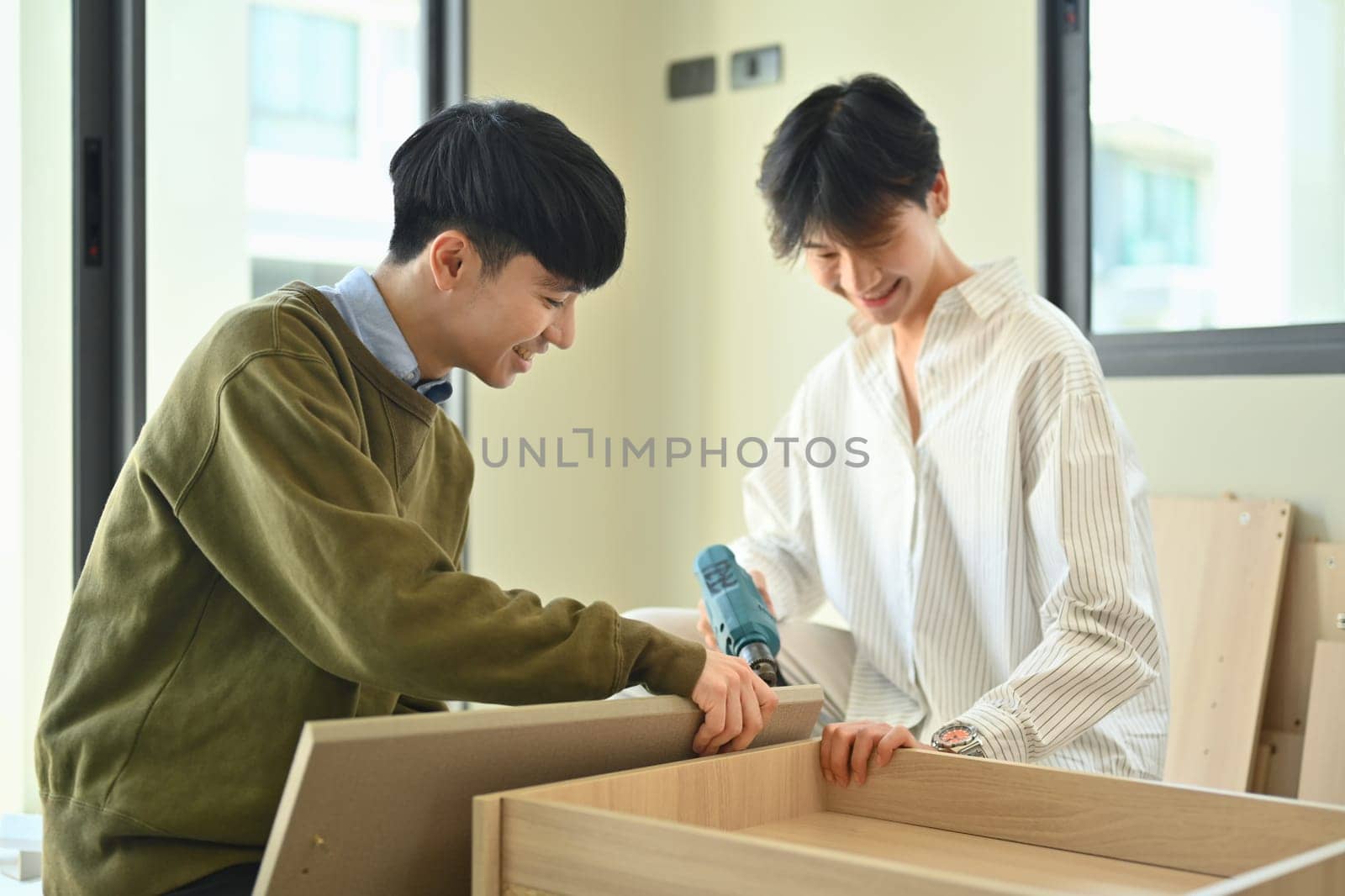 Happy asian gay couple talking and assembling furniture at their new home. LGBTQ, relocation and real estate.