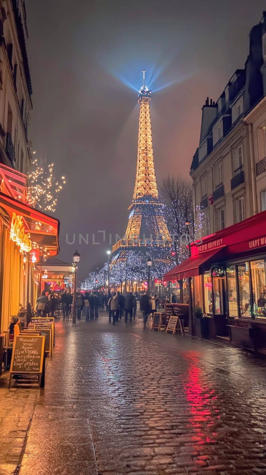 Christmas lights glowing on eiffel tower at night with tourists walking down cobblestone street in paris, france