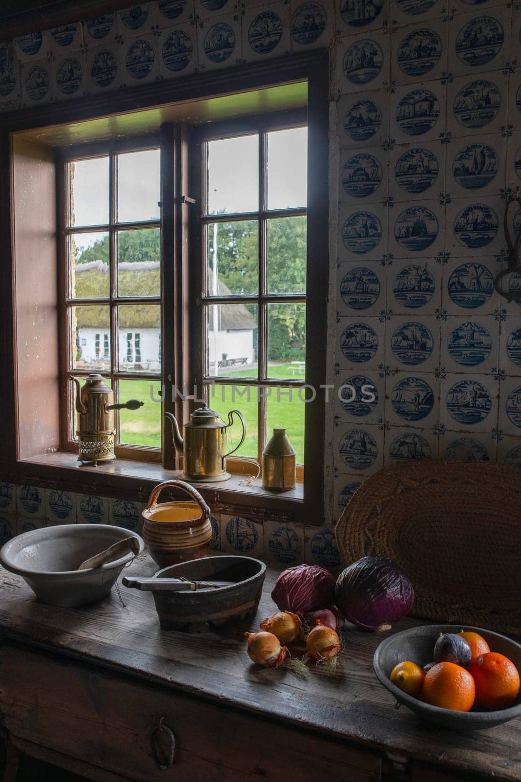 A cozy rustic kitchen with vintage utensils and fresh produce on a wooden table. A charming view through the window reveals a serene countryside setting.