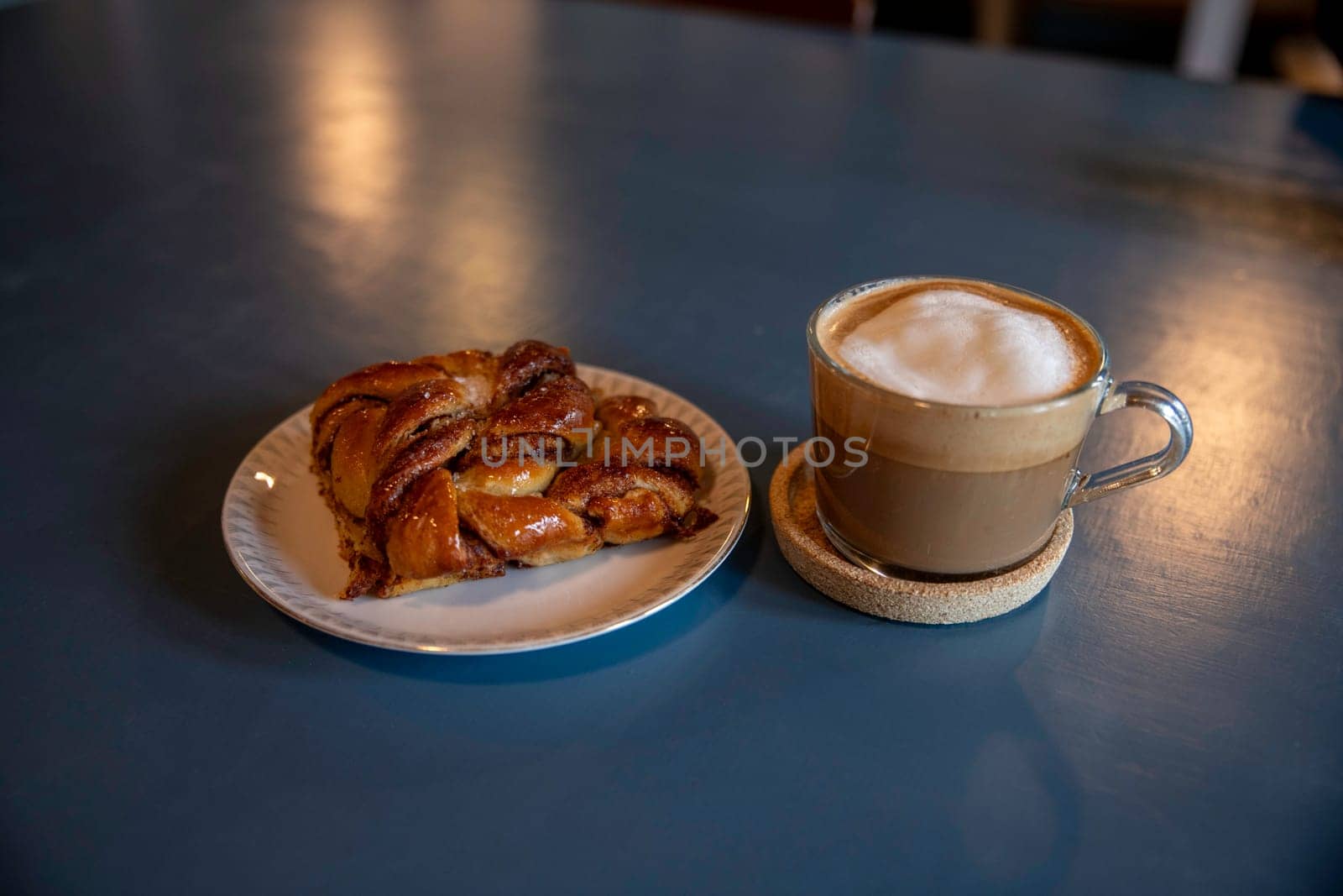 A close-up of a freshly baked cinnamon pastry served on a white plate. The warm, inviting lighting enhances its golden-brown texture, creating a cozy and appetizing atmosphere in denmark png file