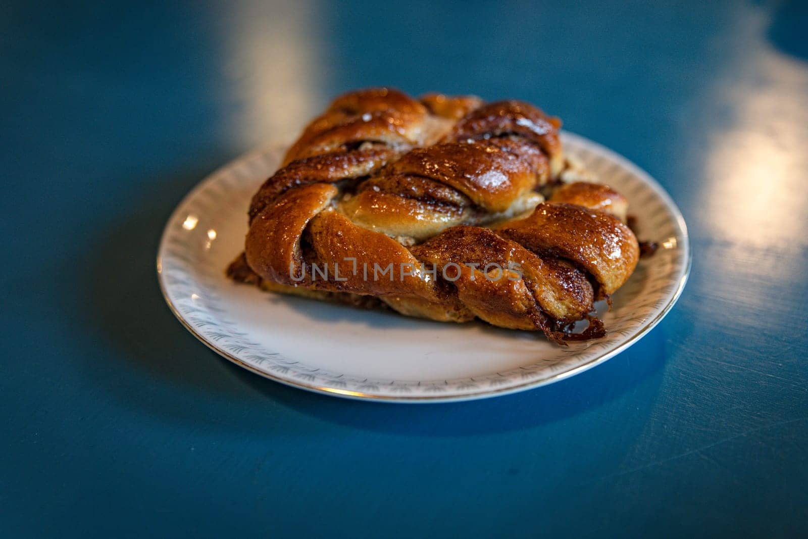 A close-up of a freshly baked cinnamon pastry served on a white plate. The warm, inviting lighting enhances its golden-brown texture, creating a cozy and appetizing atmosphere in denmark