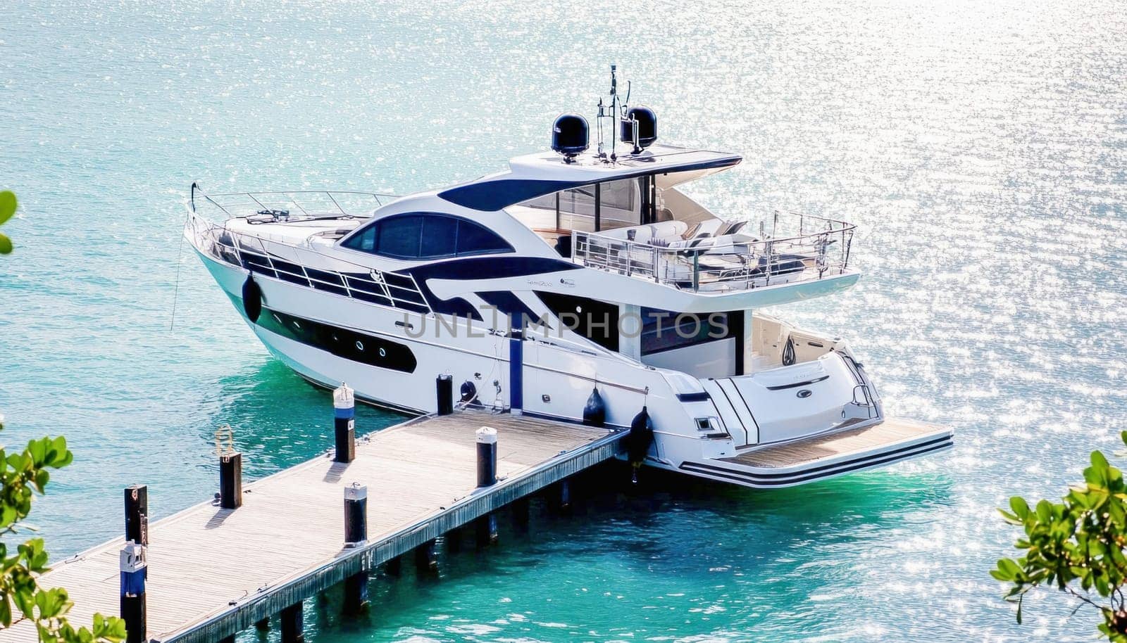 Modern white motor yacht is moored to a wooden pier in calm turquoise waters, bathed in sunlight