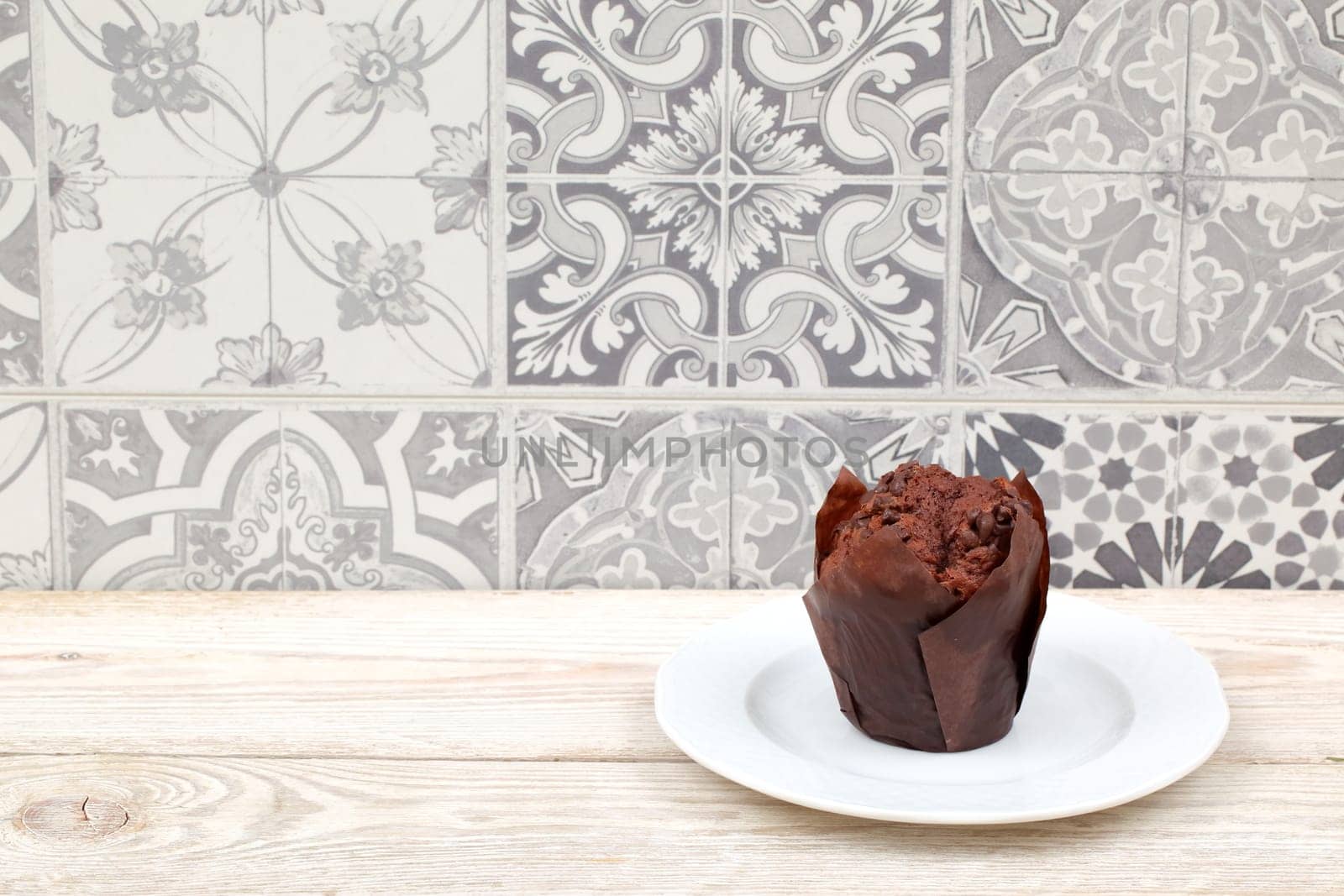 A delicious chocolate muffin sits elegantly on a white plate, beautifully displayed against a patterned backdrop