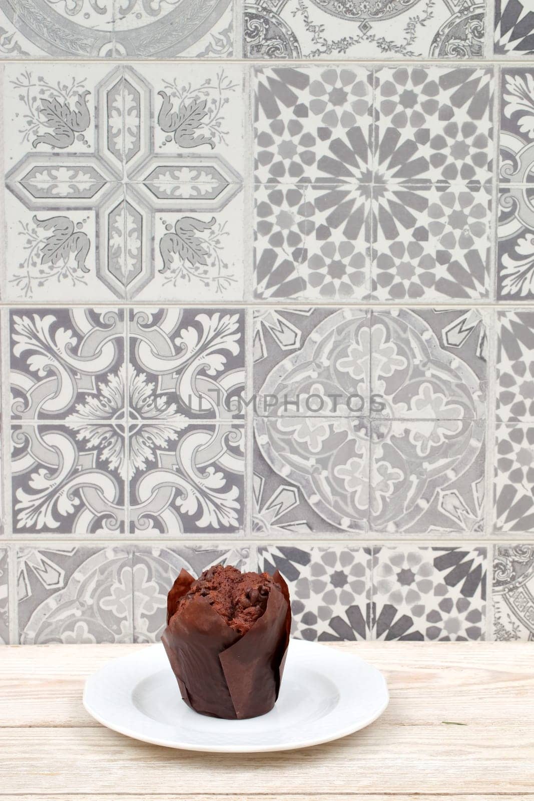 A delicious chocolate muffin elegantly served on a plate, set against a stylish patterned tile backdrop