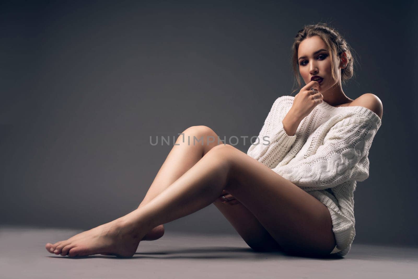 Gorgeous girl wearing only a sexy short pullover sitting on the floor full-length view in a dark room