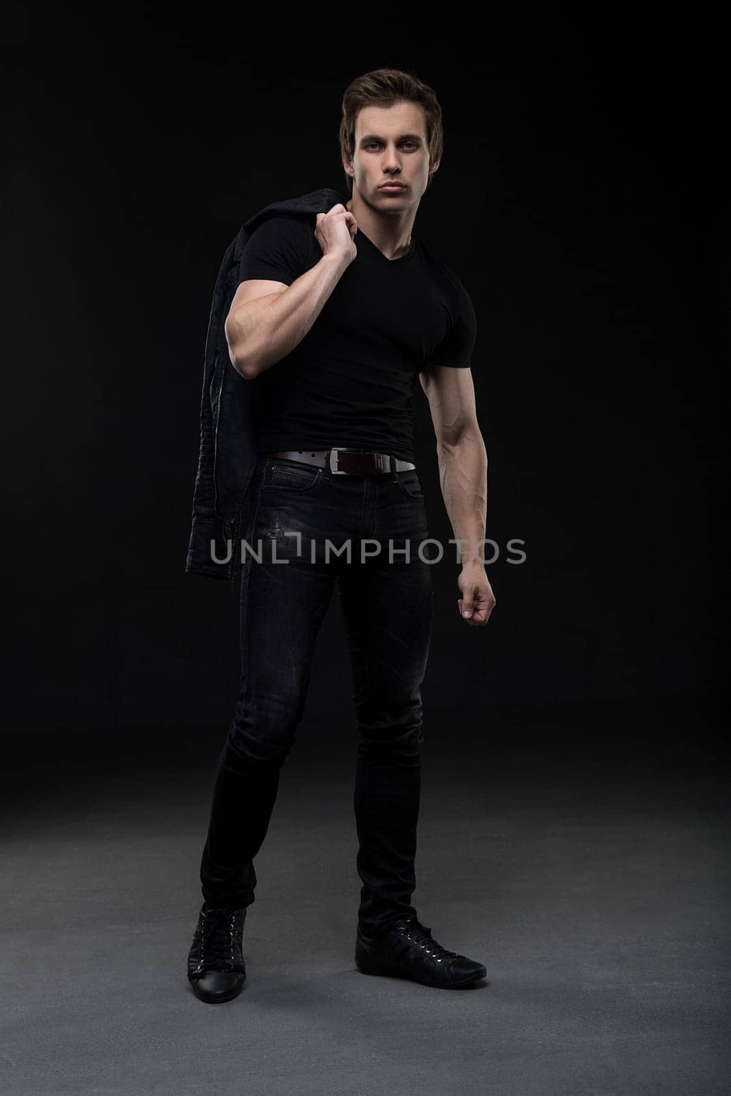 Charming sexy male in black jeanswear full-length shot in the dark room