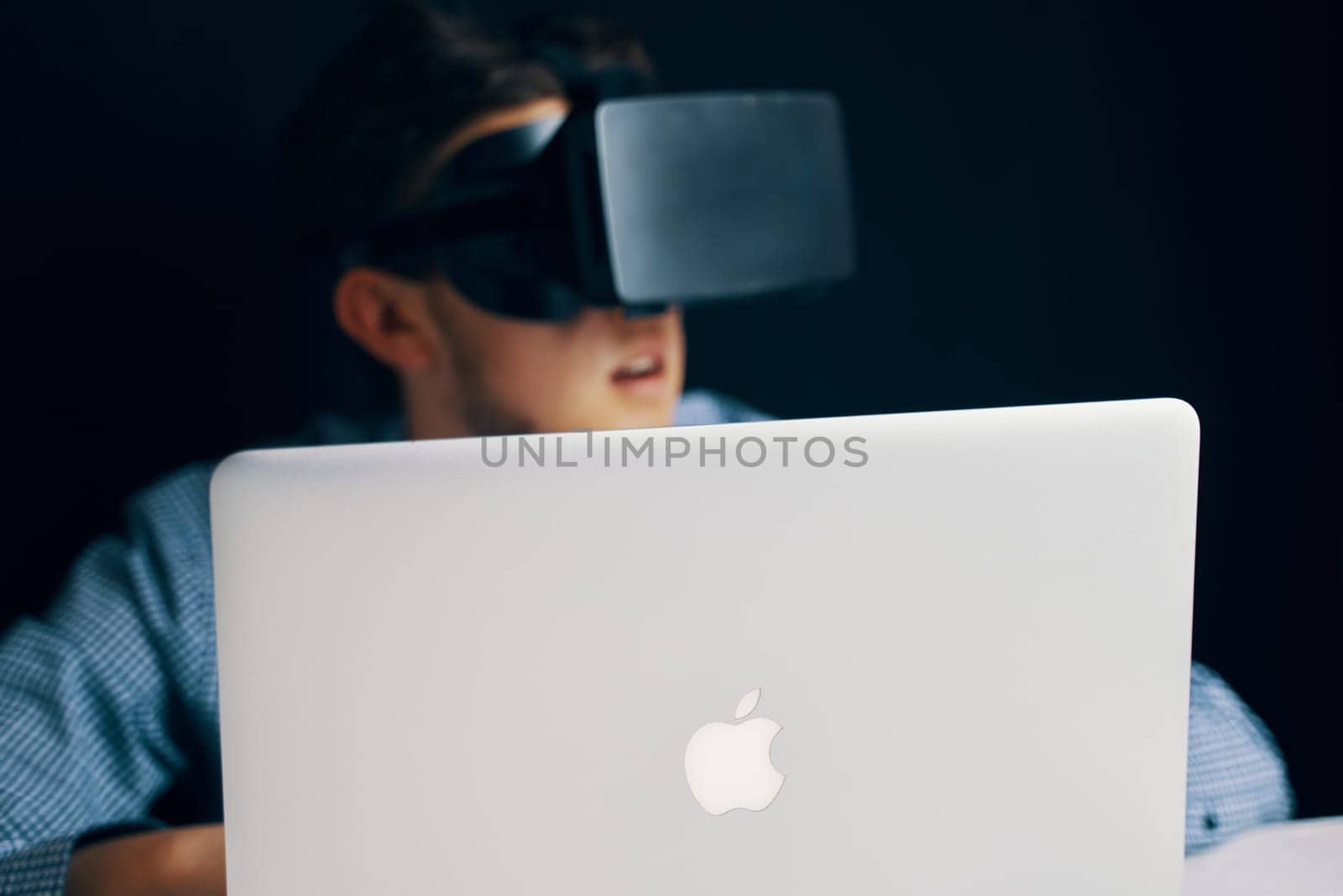 A young boy is seated in front of an Apple laptop, fully immersed in a virtual reality experience using a headset. Bishkek, Kyrgyzstan - March 14, 2020