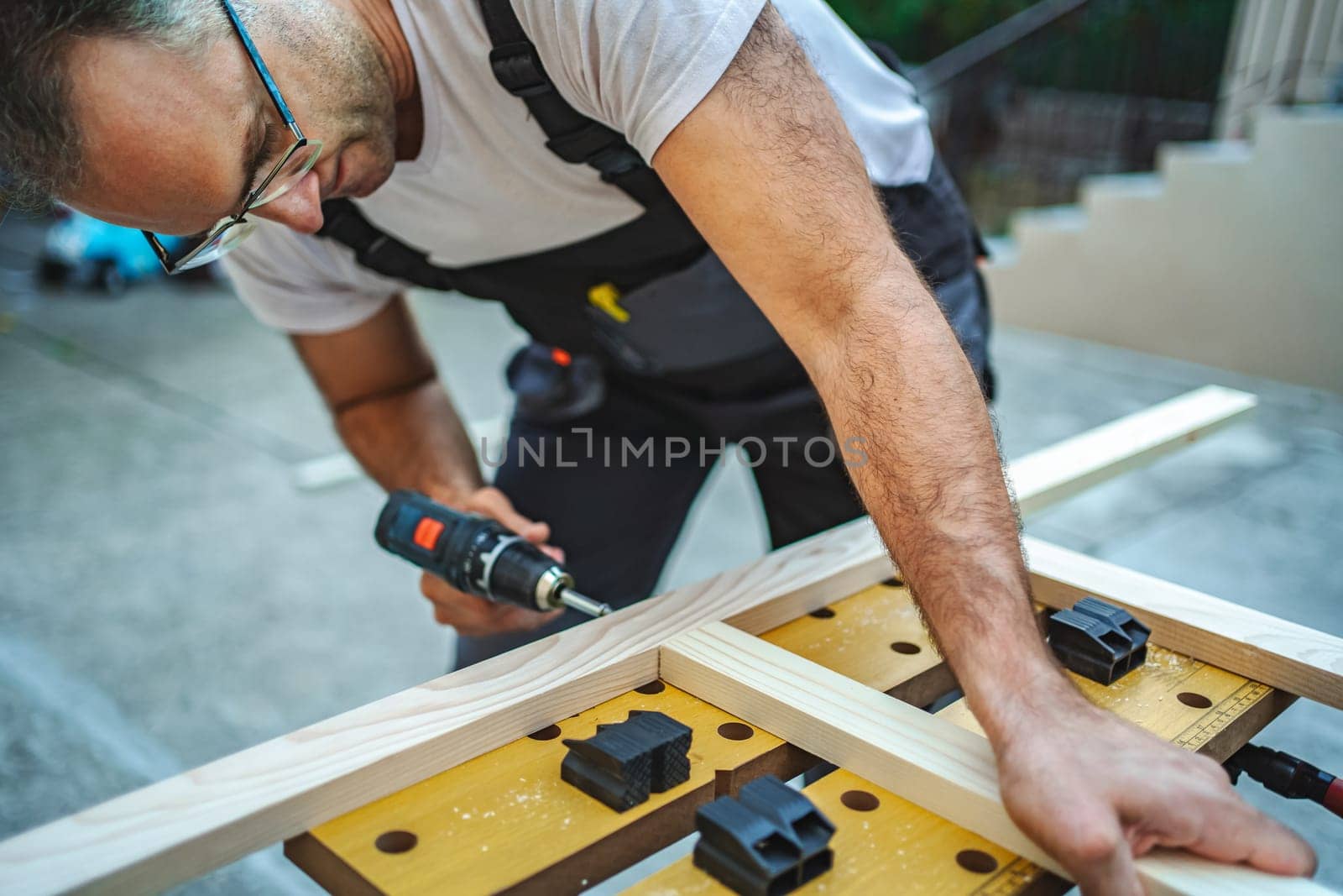 Mature male carpenter using electric screwdriver on a wooden plank outdoors.