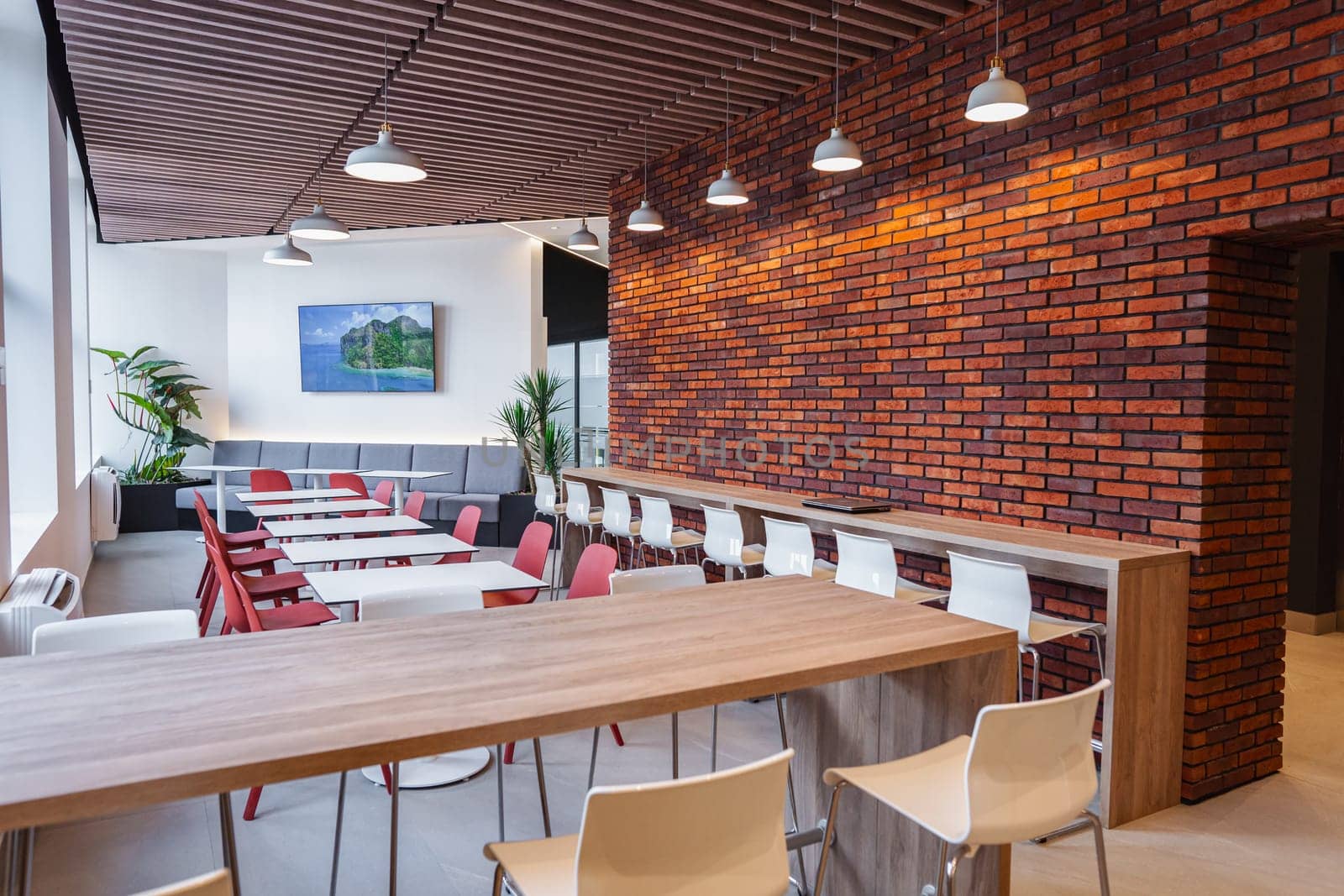 A long wooden table is lined with chairs against a brick wall, creating a simple and functional seating arrangement. The sturdy chairs are neatly arranged, ready for occupants to sit and engage in activities. The rustic brick wall adds a touch of character to the scene.
