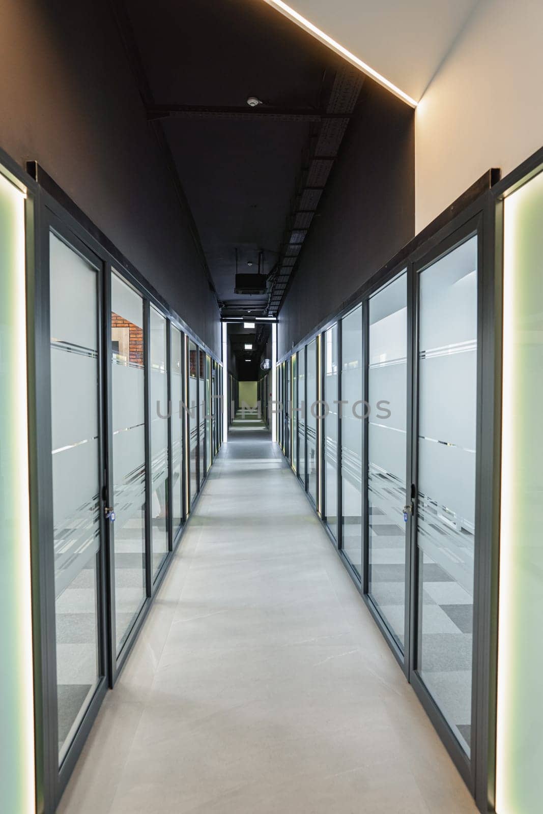 A long hallway with glass doors leading to another office. The hallway is well-lit, highlighting the clean design and architecture of the space. The glass doors offer a glimpse into the next room, creating a sense of continuity and connection in the building.