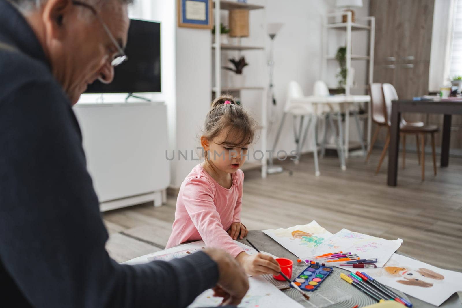 A grandfather shares a joyful moment painting with his granddaughter.
