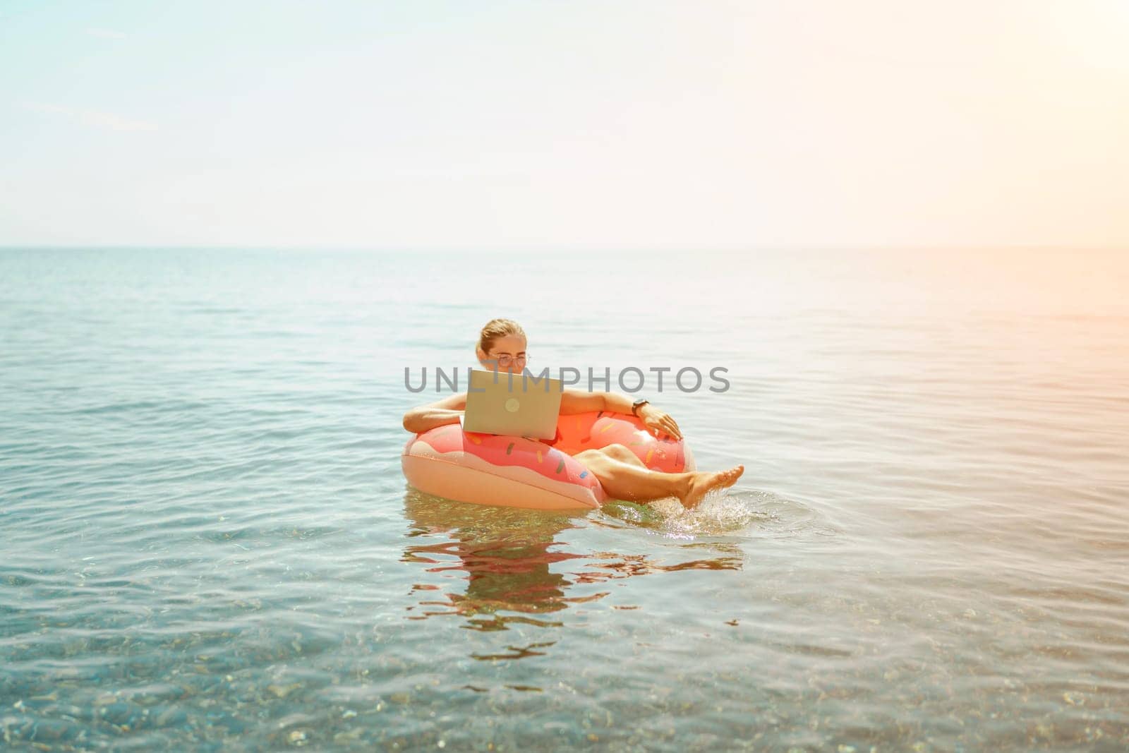 Woman laptop sea. Freelancer woman in sunglases floating on an inflatable big pink donut with a laptop in the sea. People summer vacation rest lifestyle concept