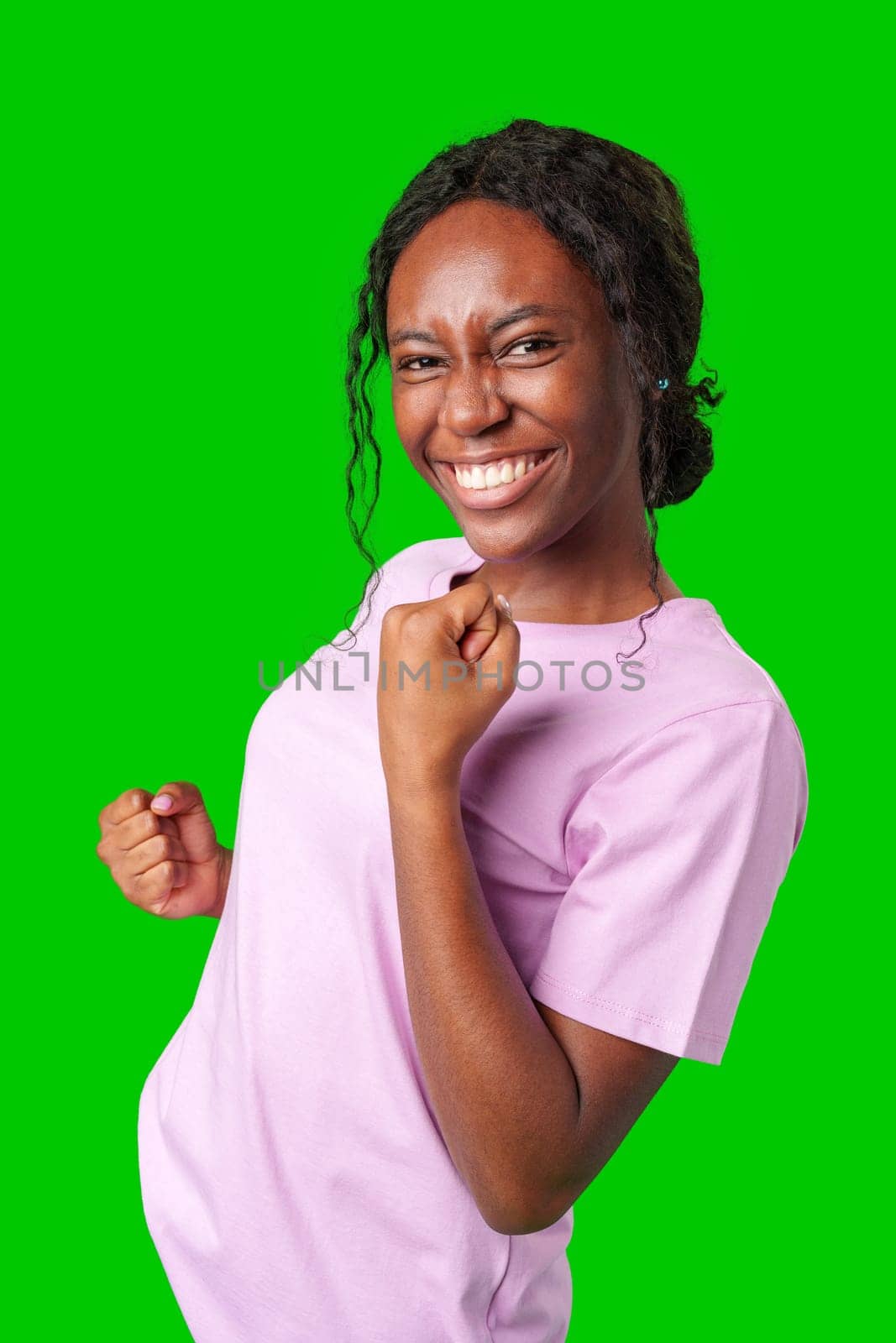 Joyful woman celebrating success with clenched fists against a bright green background close up