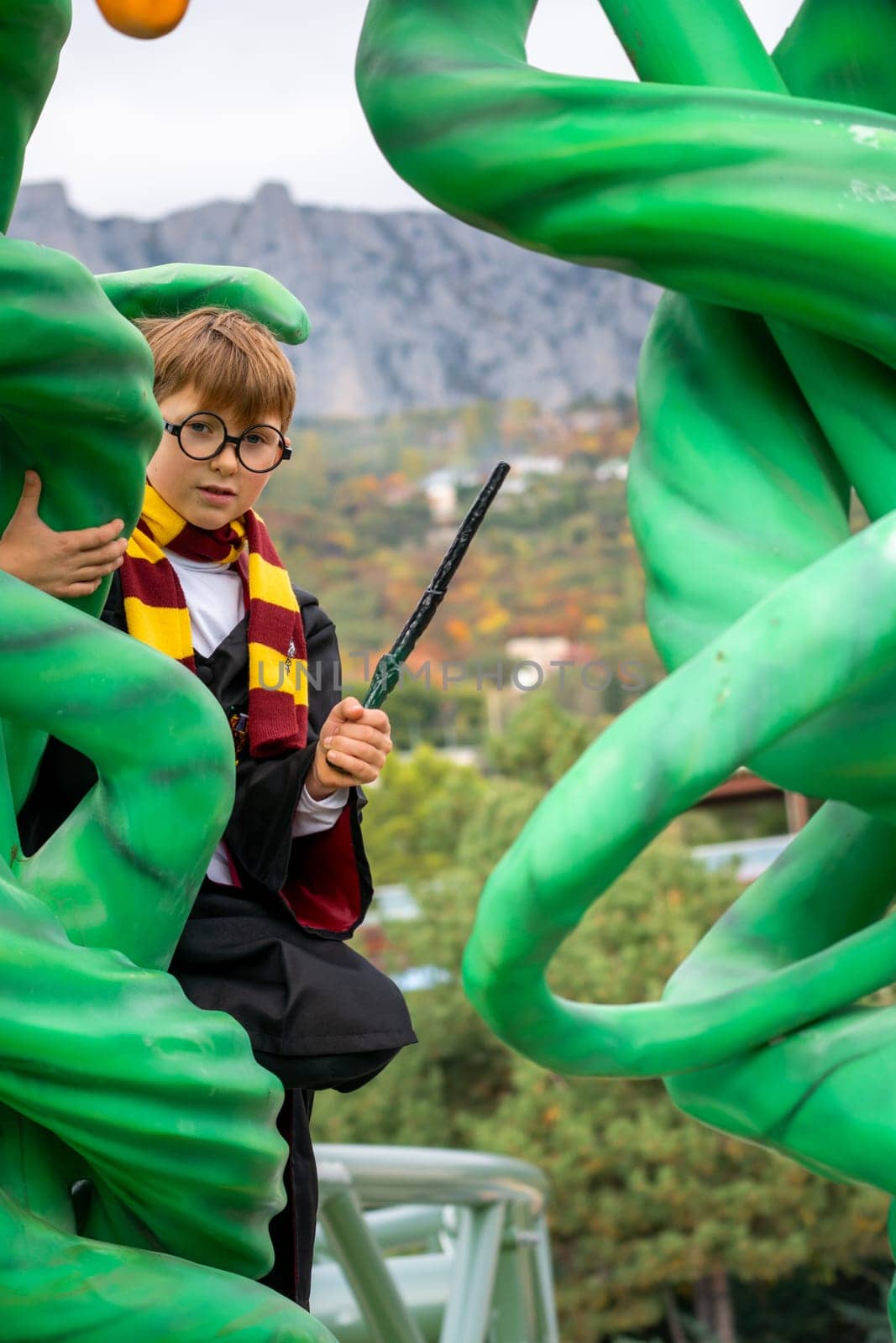 A young wizard, dressed in Gryffindor robes and holding a wand, sits atop a large green, twisting structure, seemingly made of vines.