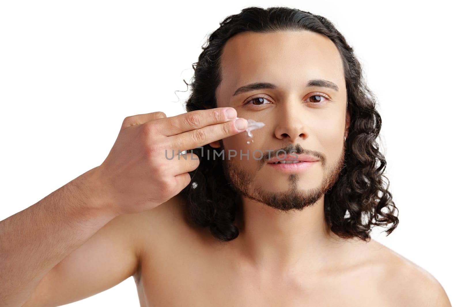 A young man demonstrates skincare routine with moisturizer on his face close up