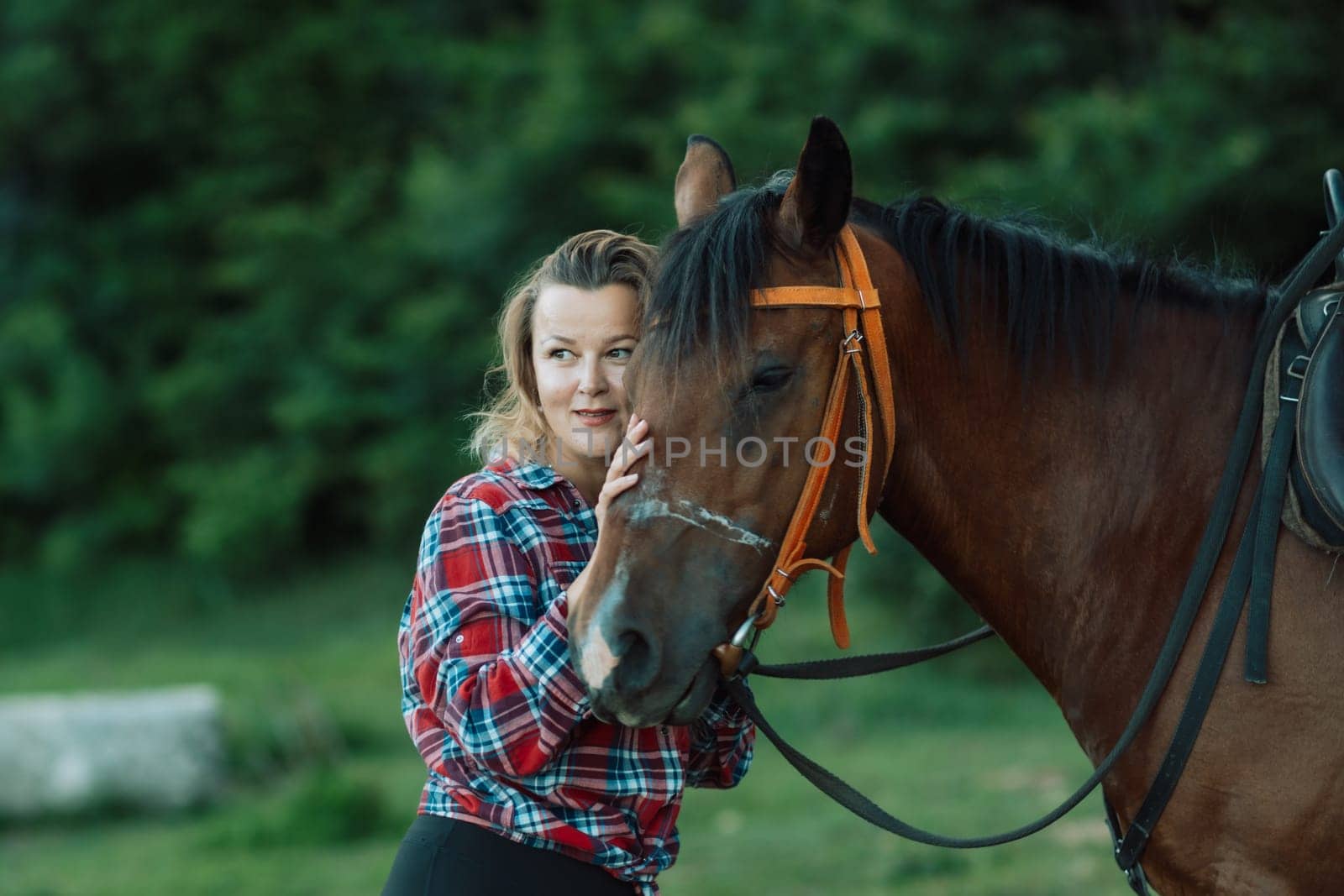Happy blonde with horse in forest. Woman and a horse walking through the field during the day. Dressed in a plaid shirt and black leggings