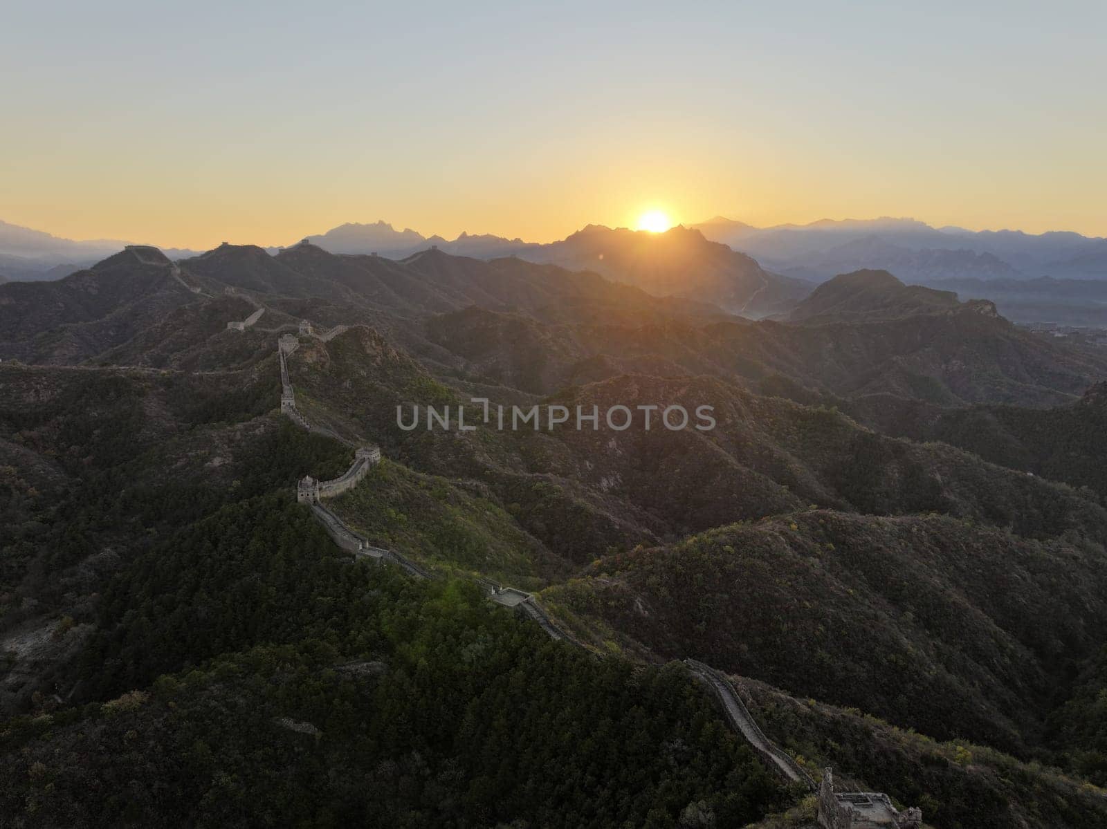 The sun rises over the rolling hills of the Great Wall of China as the manmade structure snakes along the landscape