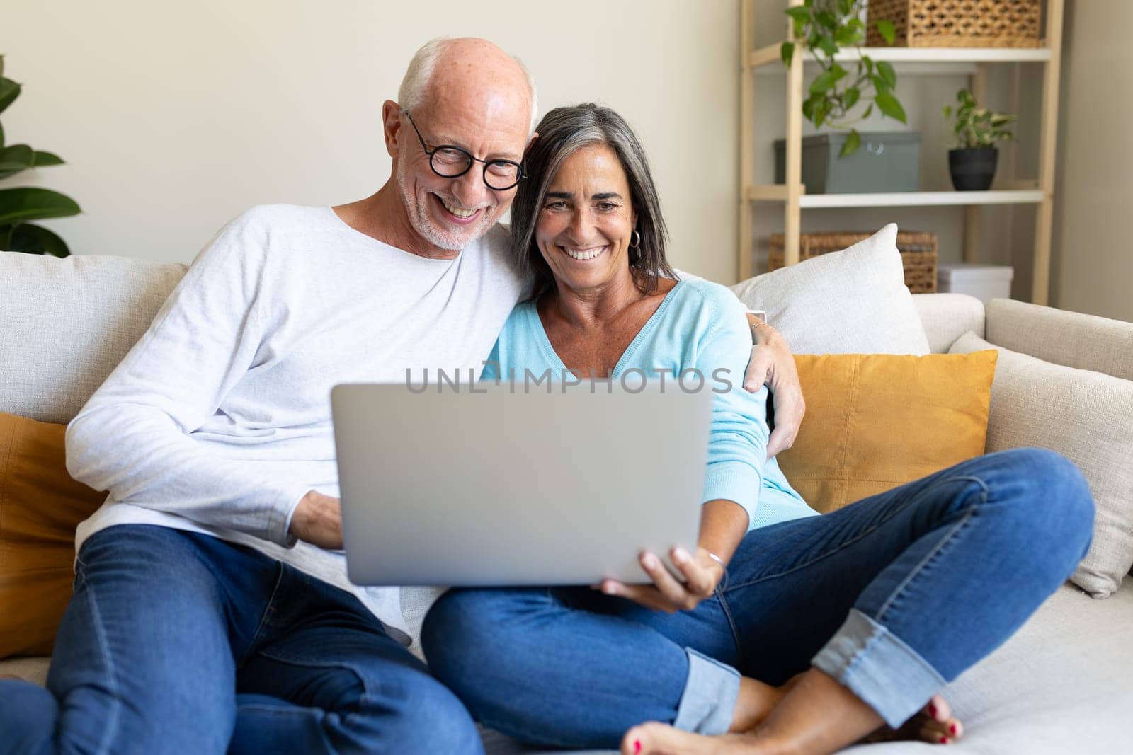 Mature happy caucasian couple using laptop at home relaxing on the sofa. Lifestyle and technology concepts.