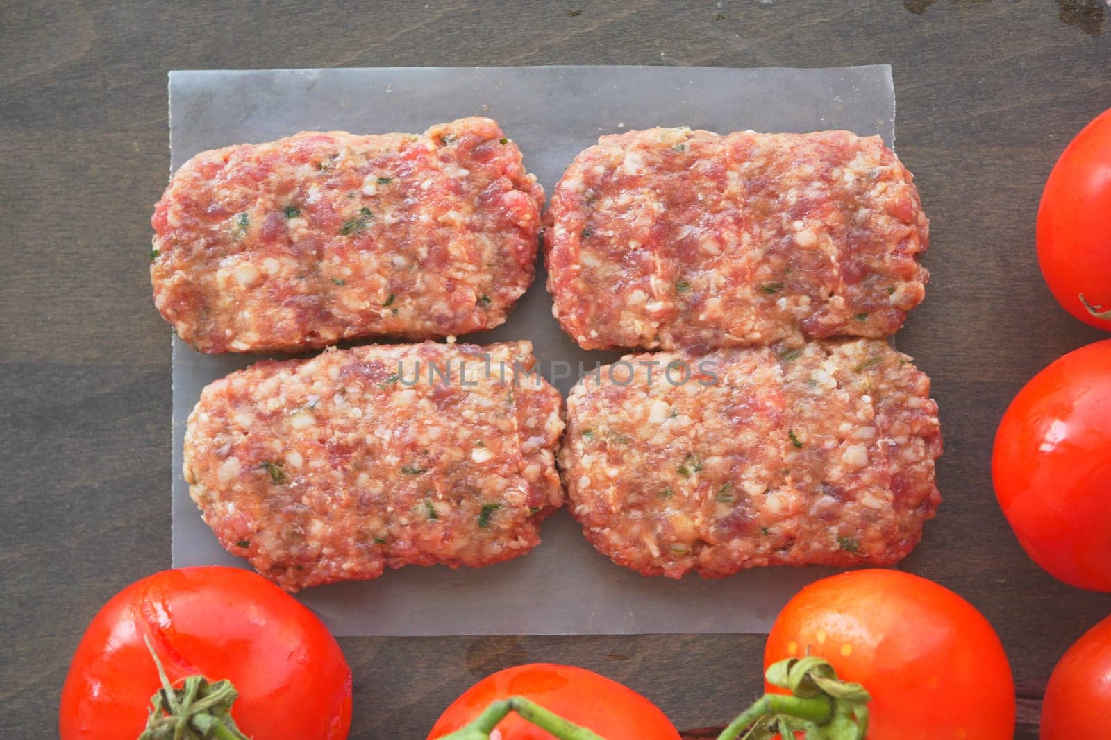 Freshly prepared meat patties, paired with succulent ripe tomatoes, are now ready for cooking