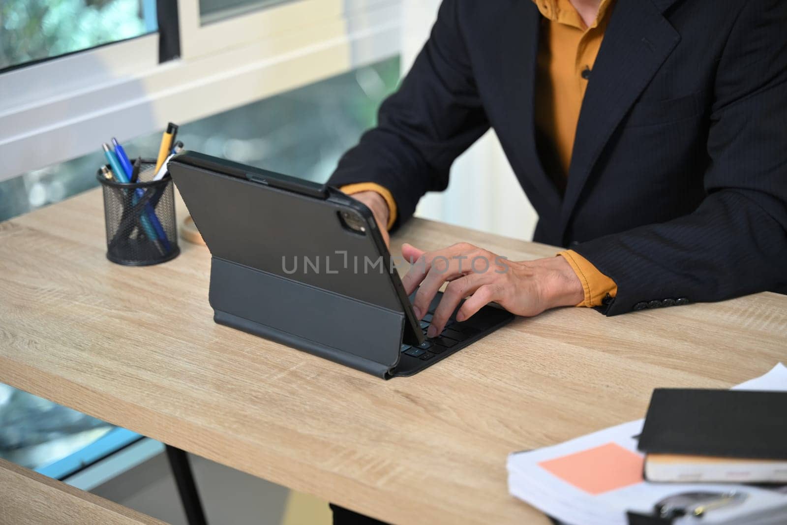 Cropped shot adult entrepreneur using digital tablet on wooden desk in office.