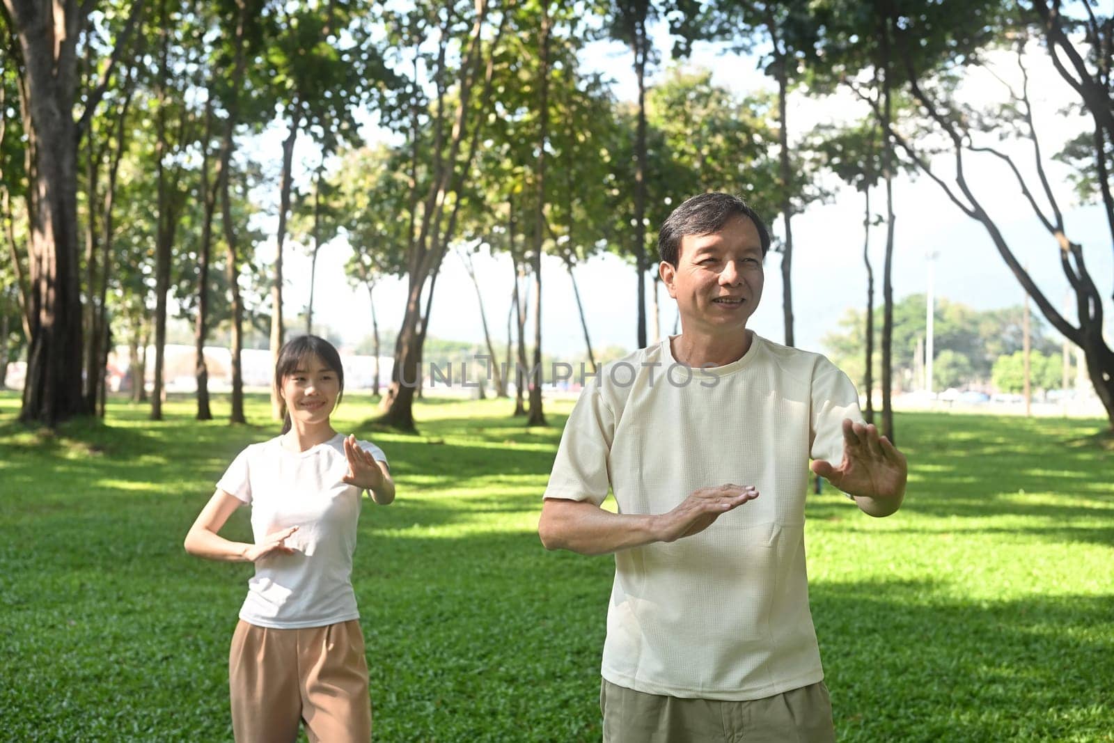 Calm father and daughter practicing Tai Chi in a serene park. Family activities, health and well being concept.