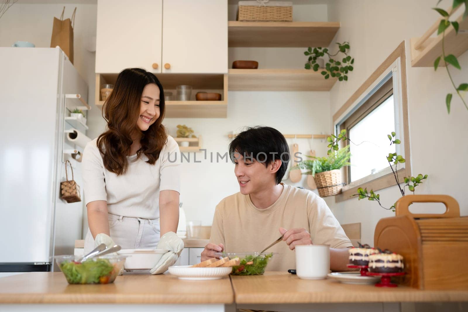 Cheerful asian woman serving healthy lunch to her husband in a minimalist kitchen.