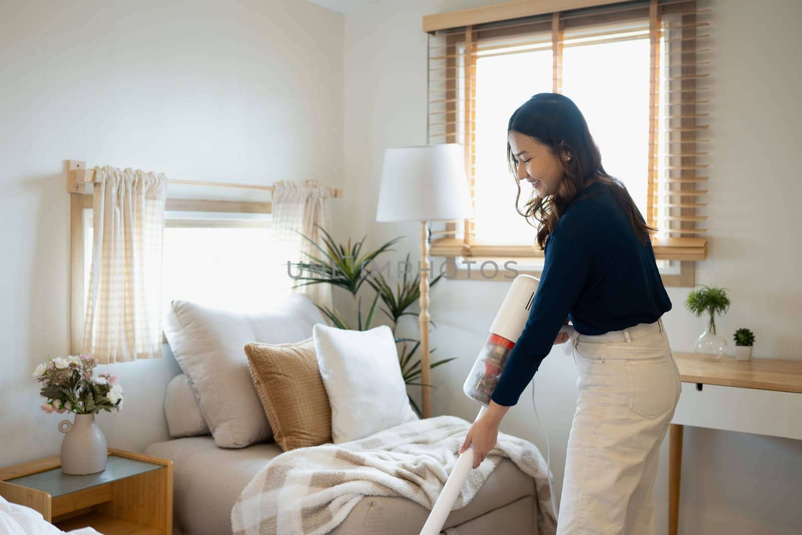 Cheerful young woman using a cordless vacuuming floor in living room.