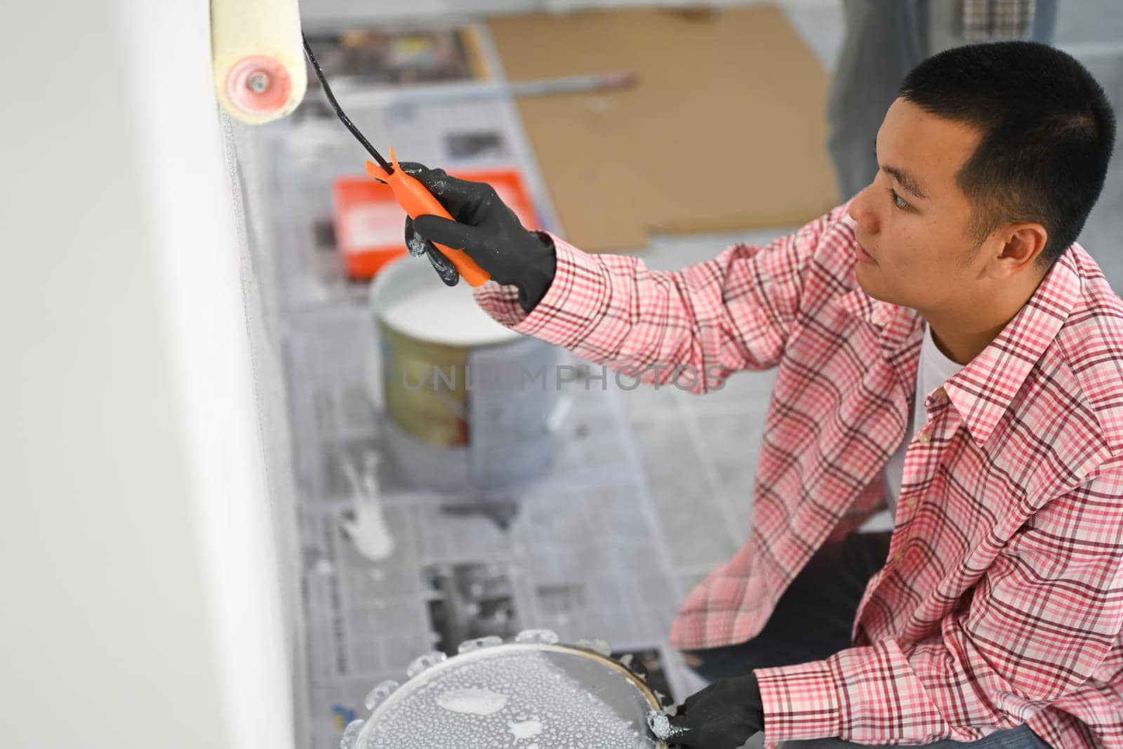 Close up of man painting a wall with a roller brush. DIY renovations and home improvement concept.
