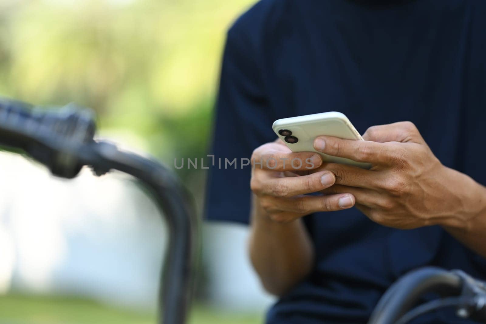 Close up young man using smartphone while sitting at the park with bicycle.