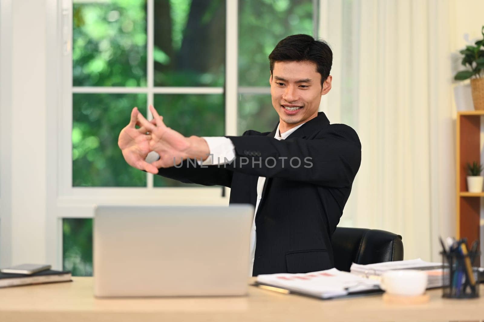 Relaxed businessman stretching after work session in the workplace.