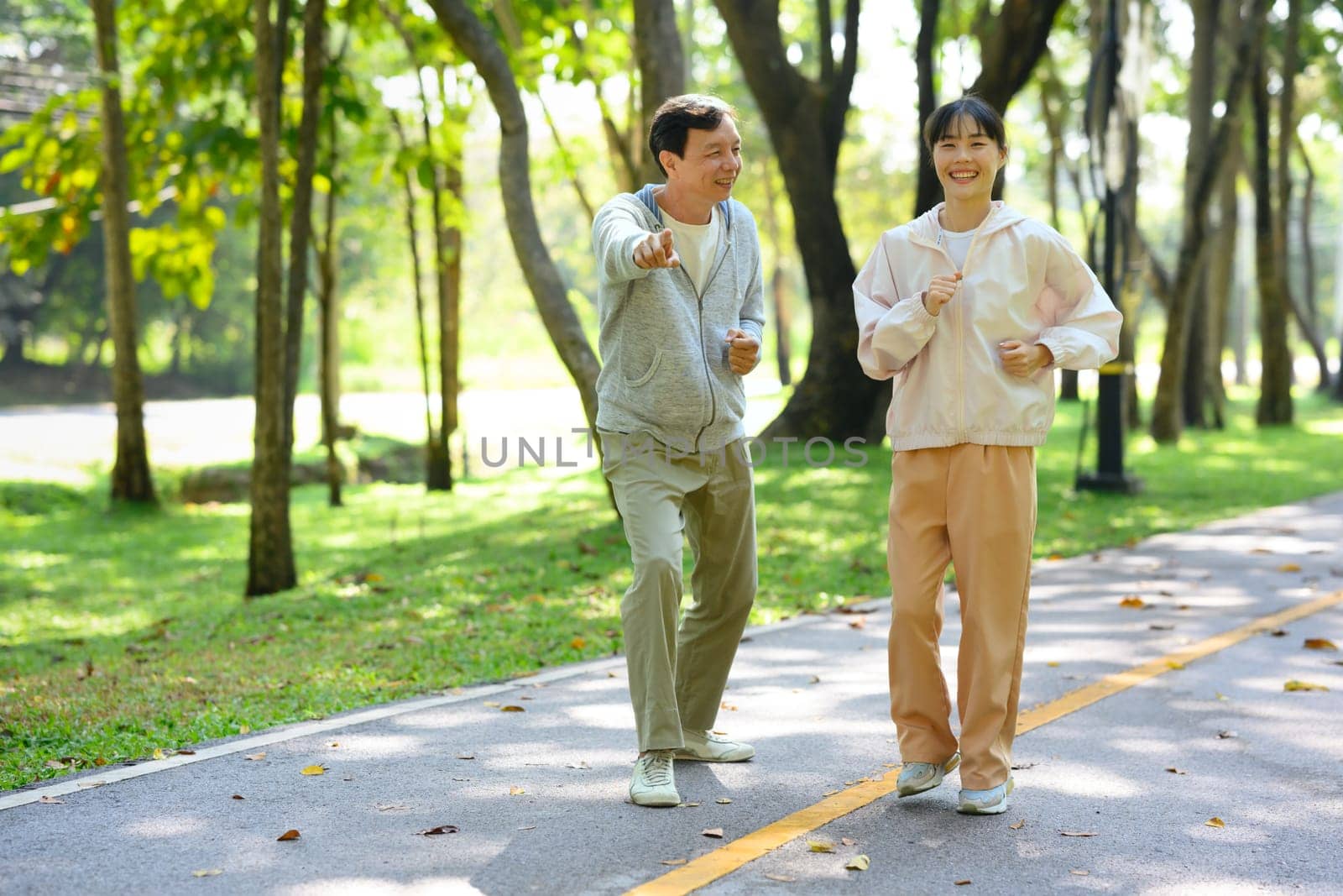 Cheerful young asian woman jogging with her father in park. Family activities, health and wellbeing concept.