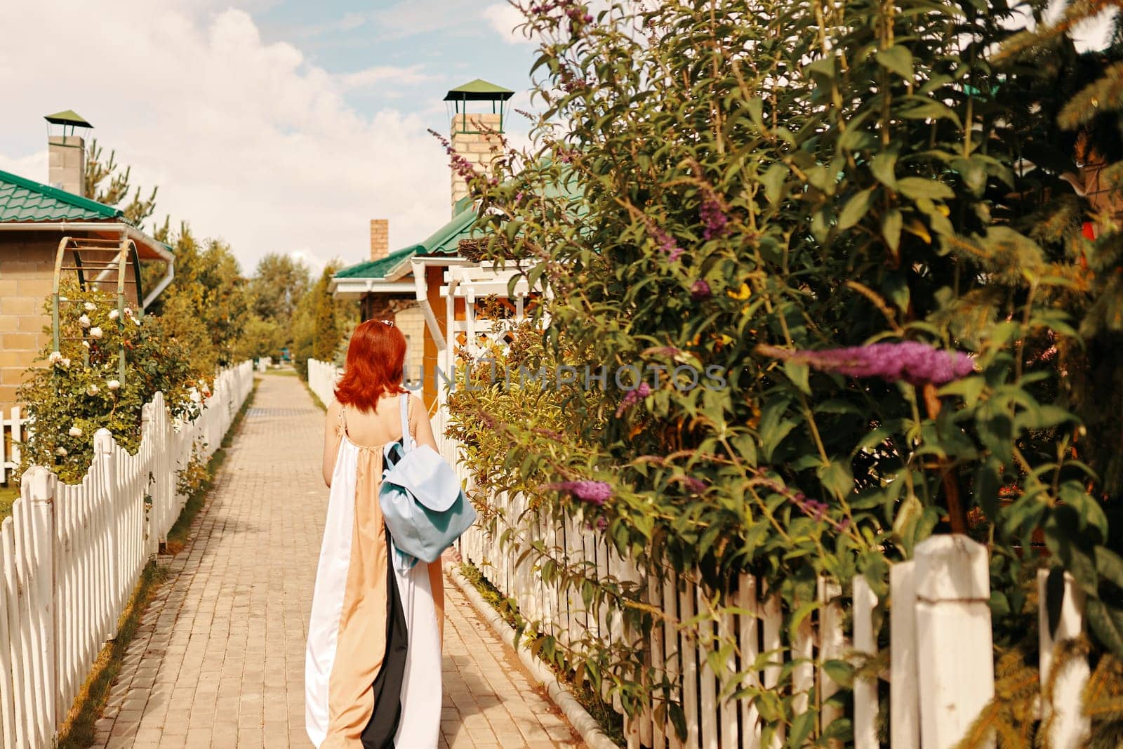 A woman carrying a backpack strolls leisurely along a picturesque pathway that is beautifully lined with lush greenery