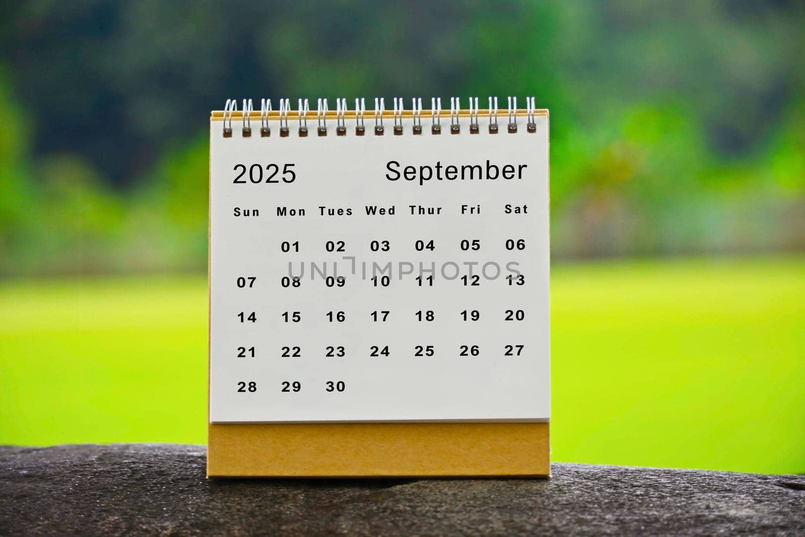 September 2025 white calendar with green blurred background.