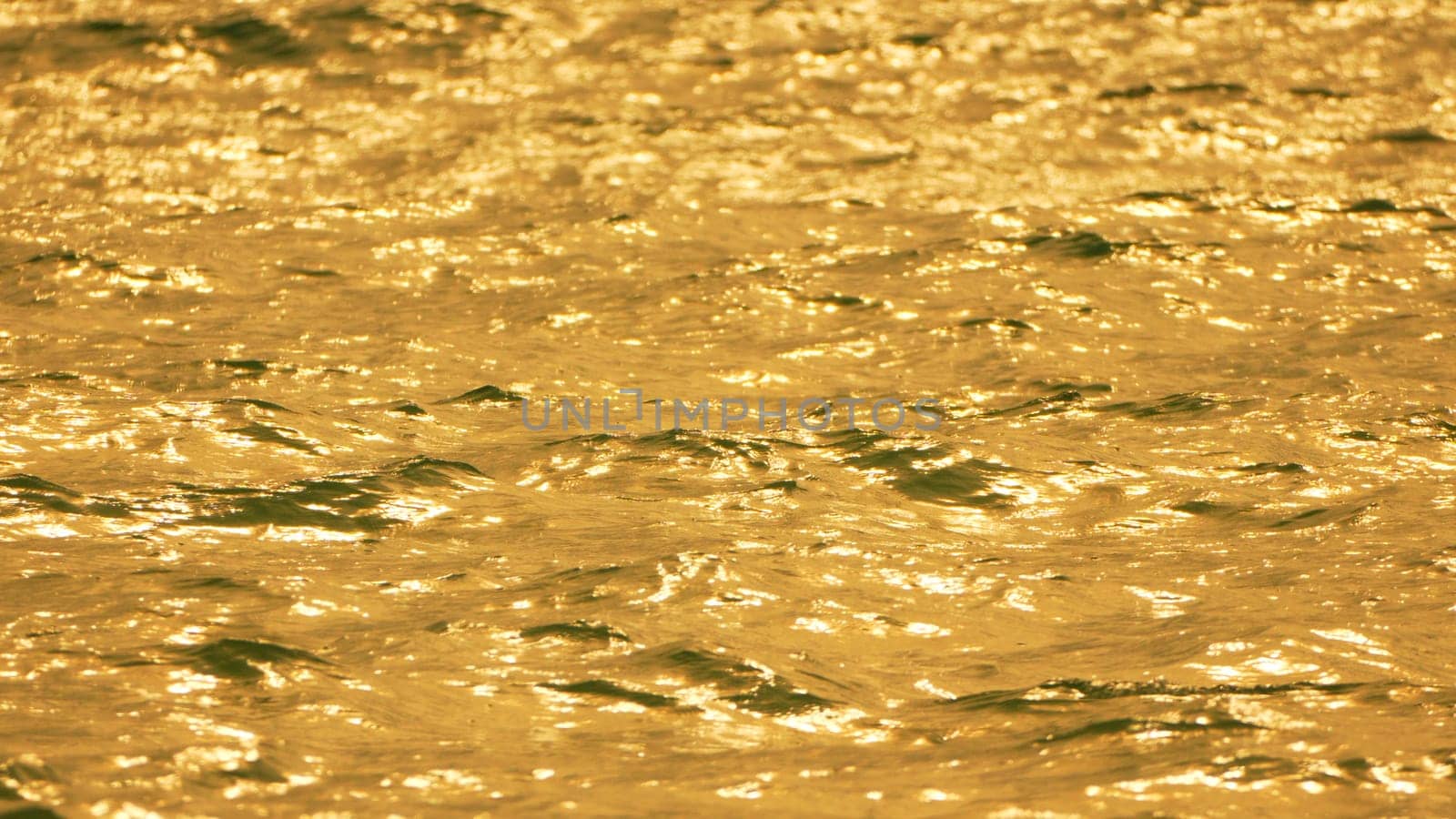 Close-up of golden, rippling water reflecting sunlight. The surface is textured and shimmering, creating a dynamic visual.
