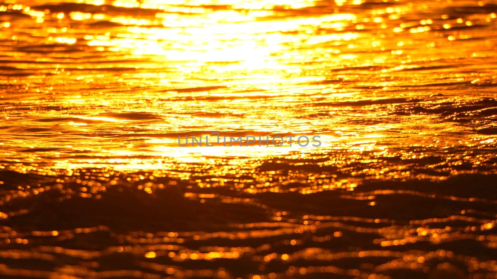 A close-up shot of molten metal, glowing intensely with a fiery orange hue. The surface is rippling and bubbling, indicating extreme heat.
