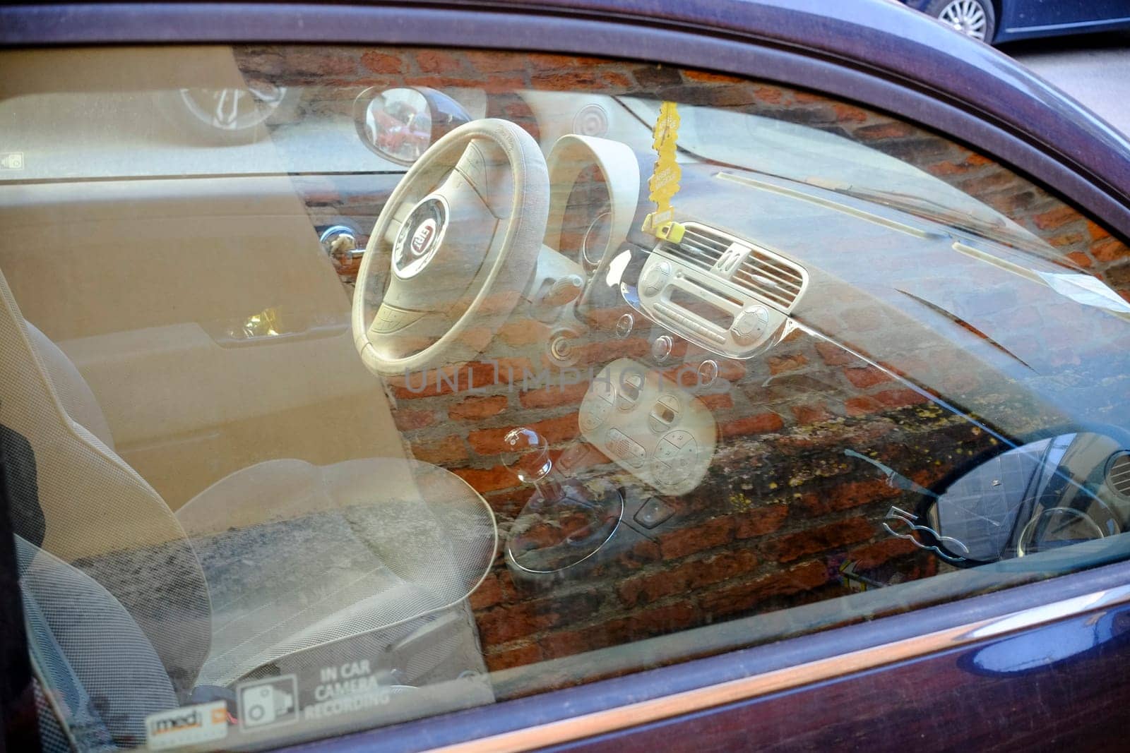 Cremona, Itally - October 6th 2024 Interior of a dusty fiat 500 lounge with beige decor, showcasing steering wheel, dashboard, gear stick, and seats against a weathered brick wall