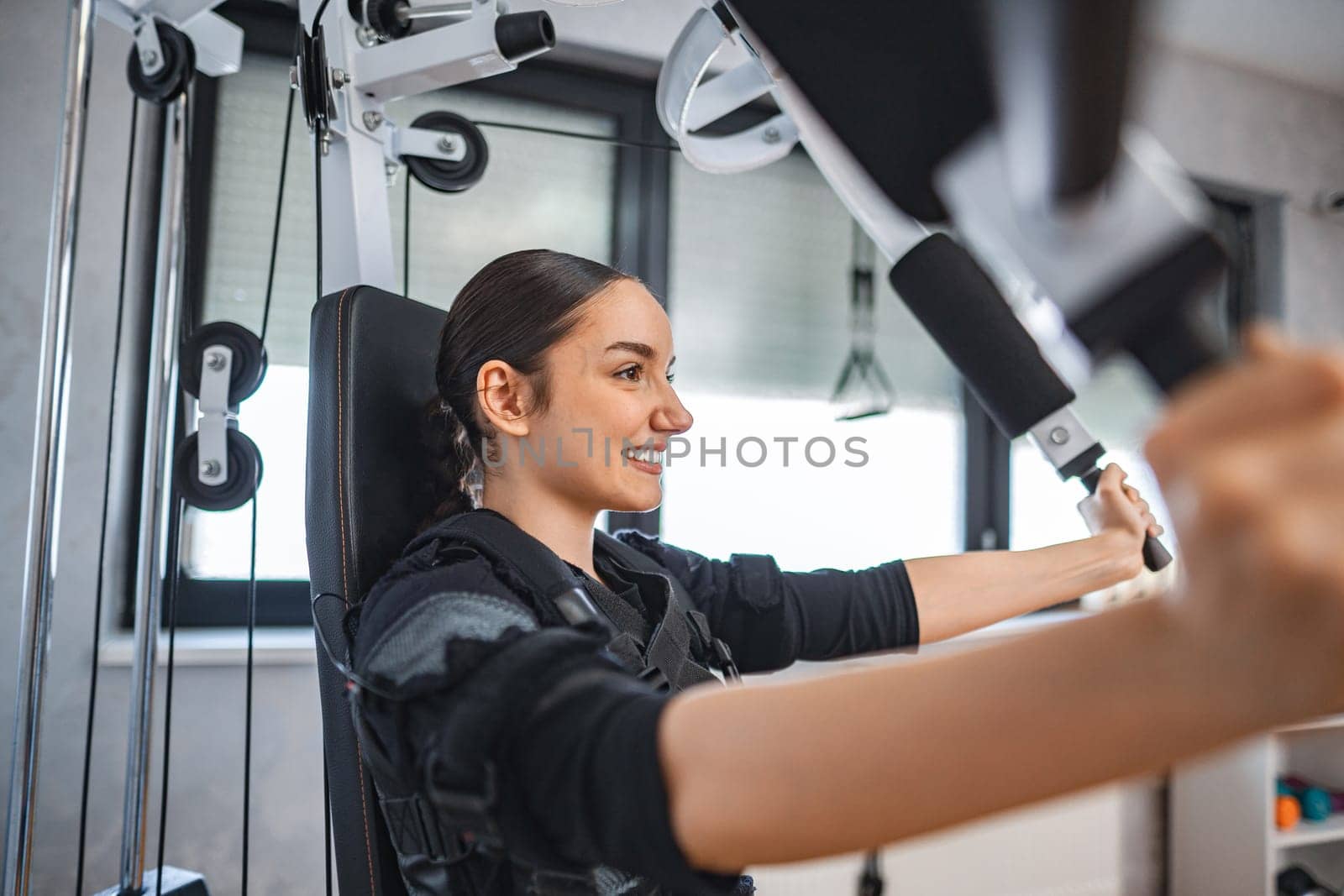 A young woman enthusiastically engages in EMS training at a fitness center.