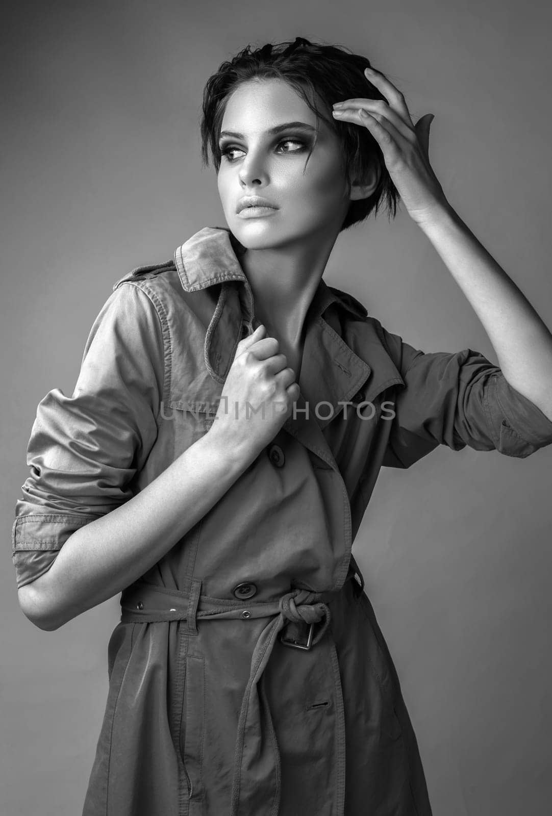 Monochrome portrait of a beautiful brunette in a studio in a raincoat