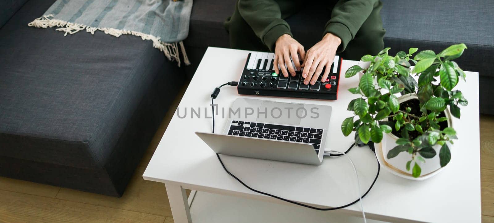 Recording electronic music track with portable midi keyboard on laptop computer in home studio. Producing and mixing music, beat making and arranging audio content with professional audio devices