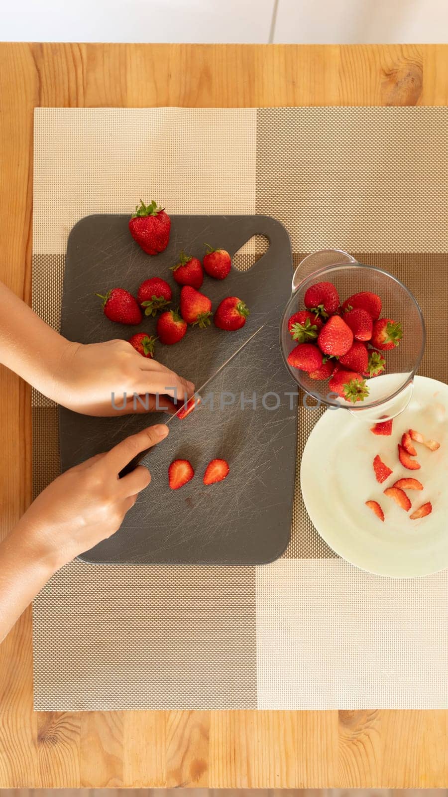 women's hands slicing strawberries on a board with a knife.