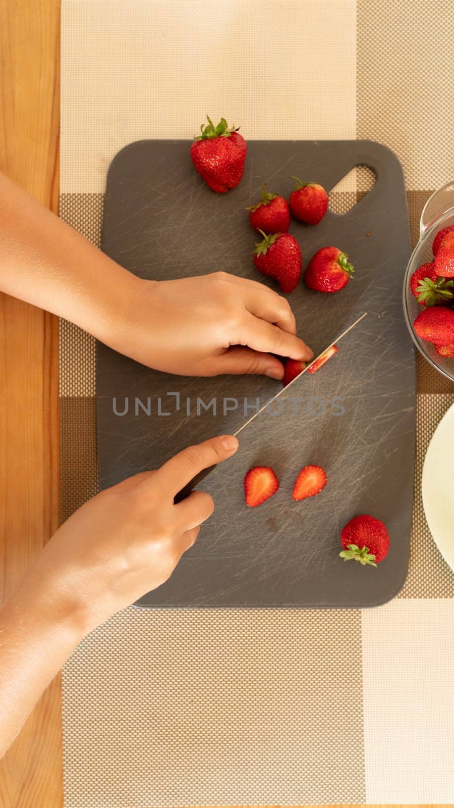 Close-up of fresh strawberries being sliced with a knife on a board in the kitchen by TRMK