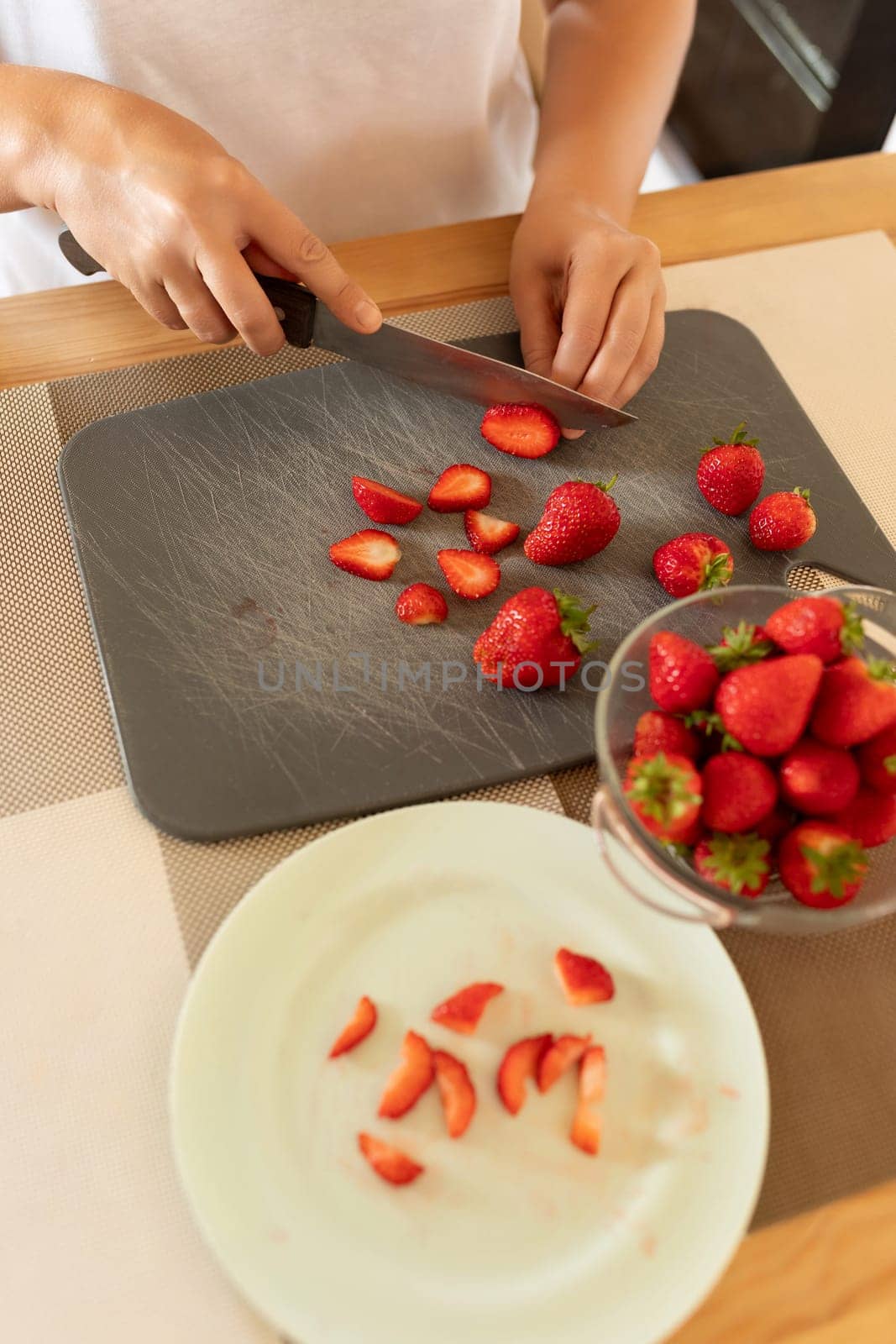 a woman slices strawberries with a knife in the kitchen.