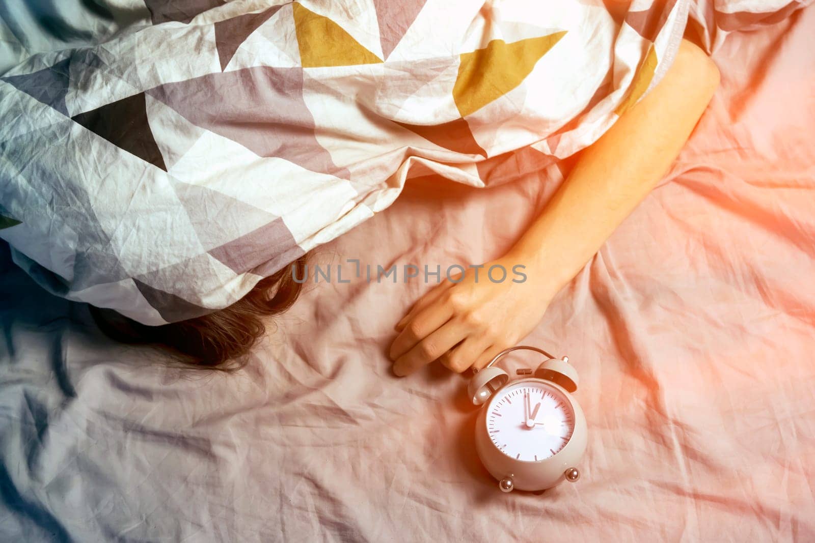 A young girl sleeps early in the morning under the blanket, a vintage alarm clock is near by her.