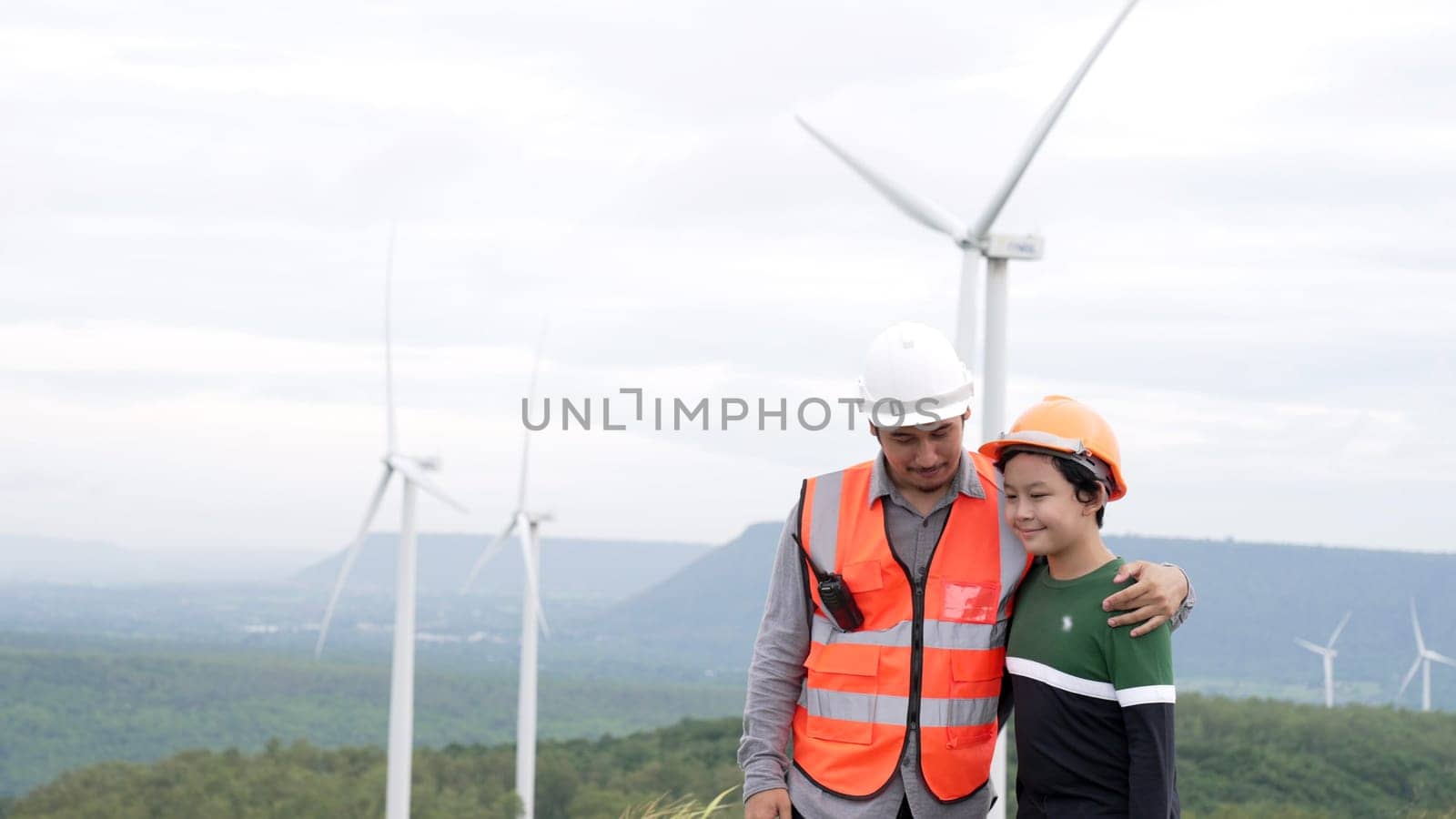 Engineer with his son on a wind farm atop a hill or mountain in the rural. Progressive ideal for the future production of renewable, sustainable energy. Energy generation from wind turbine.